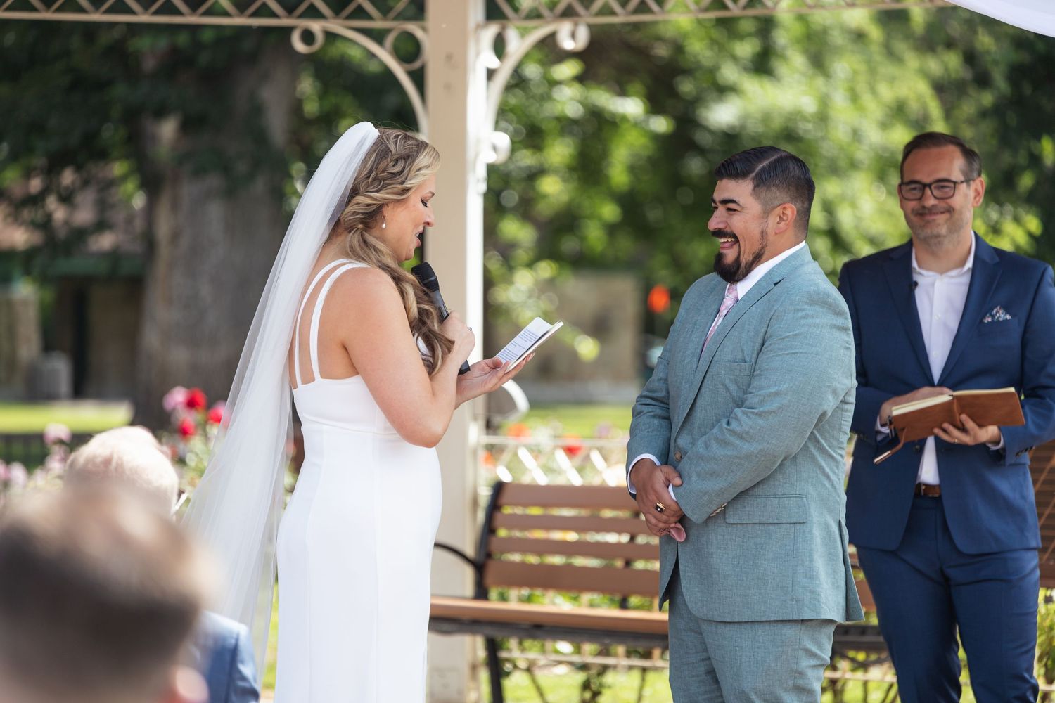 Wedding ceremony taking place under white gazebo with guests watching.