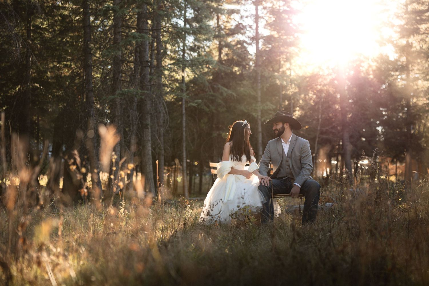 Romantic sunset portrait of newlyweds sitting in golden forest grass.