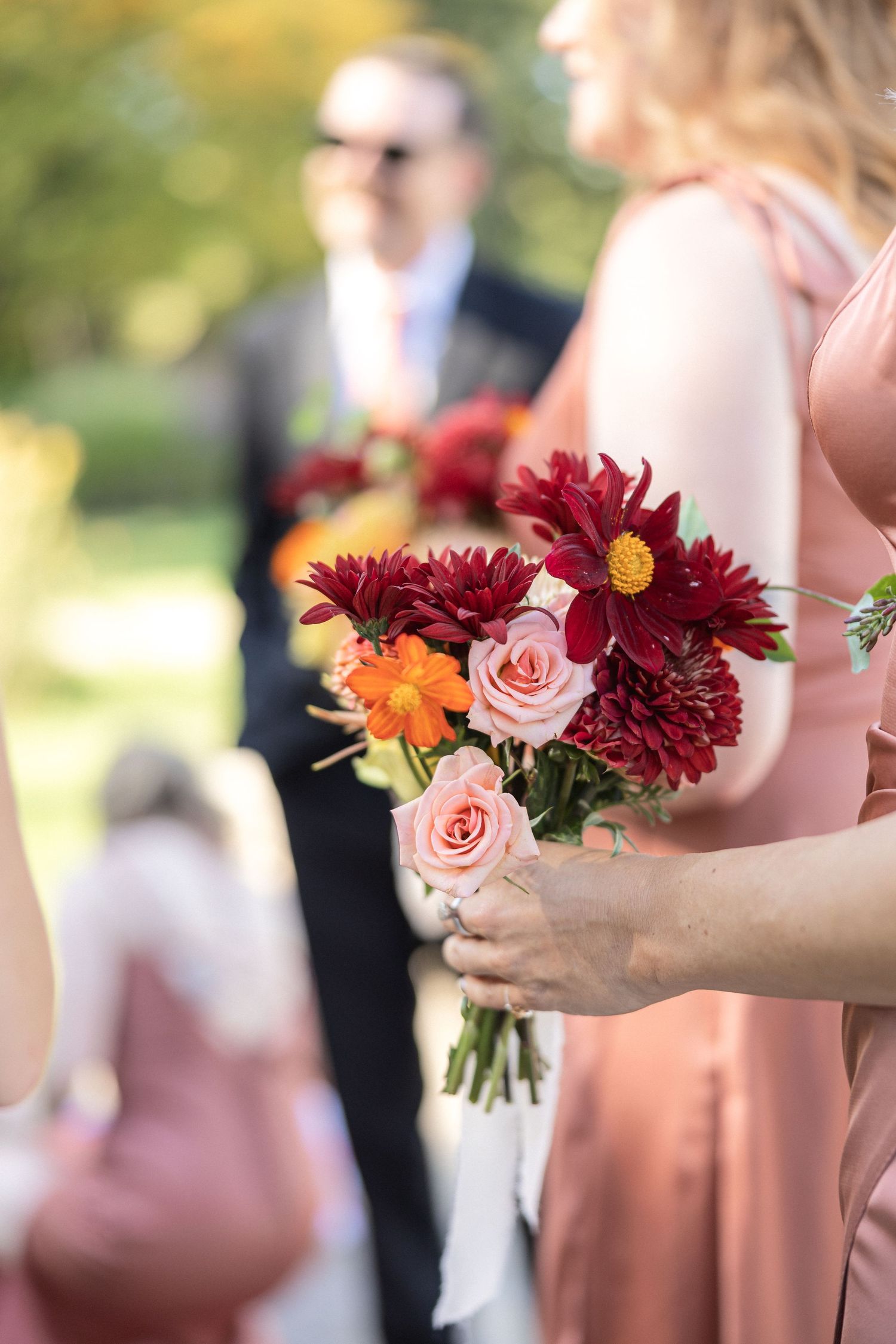 A bridesmaid holds a beautiful bouquet with burgundy dahlias and pink roses against a soft outdoor background.