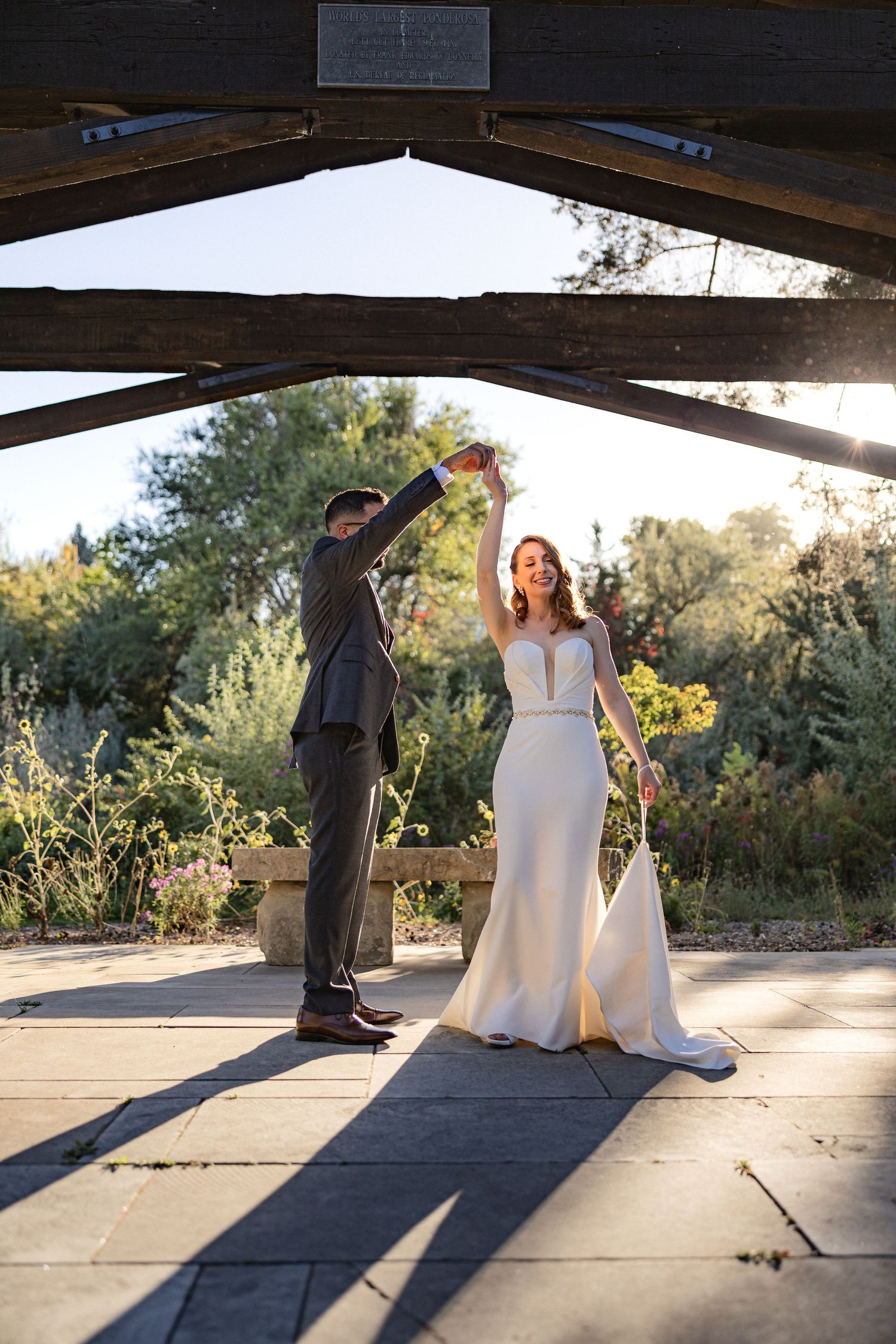 Joyful couple celebrates with raised arms under rustic wooden structure.