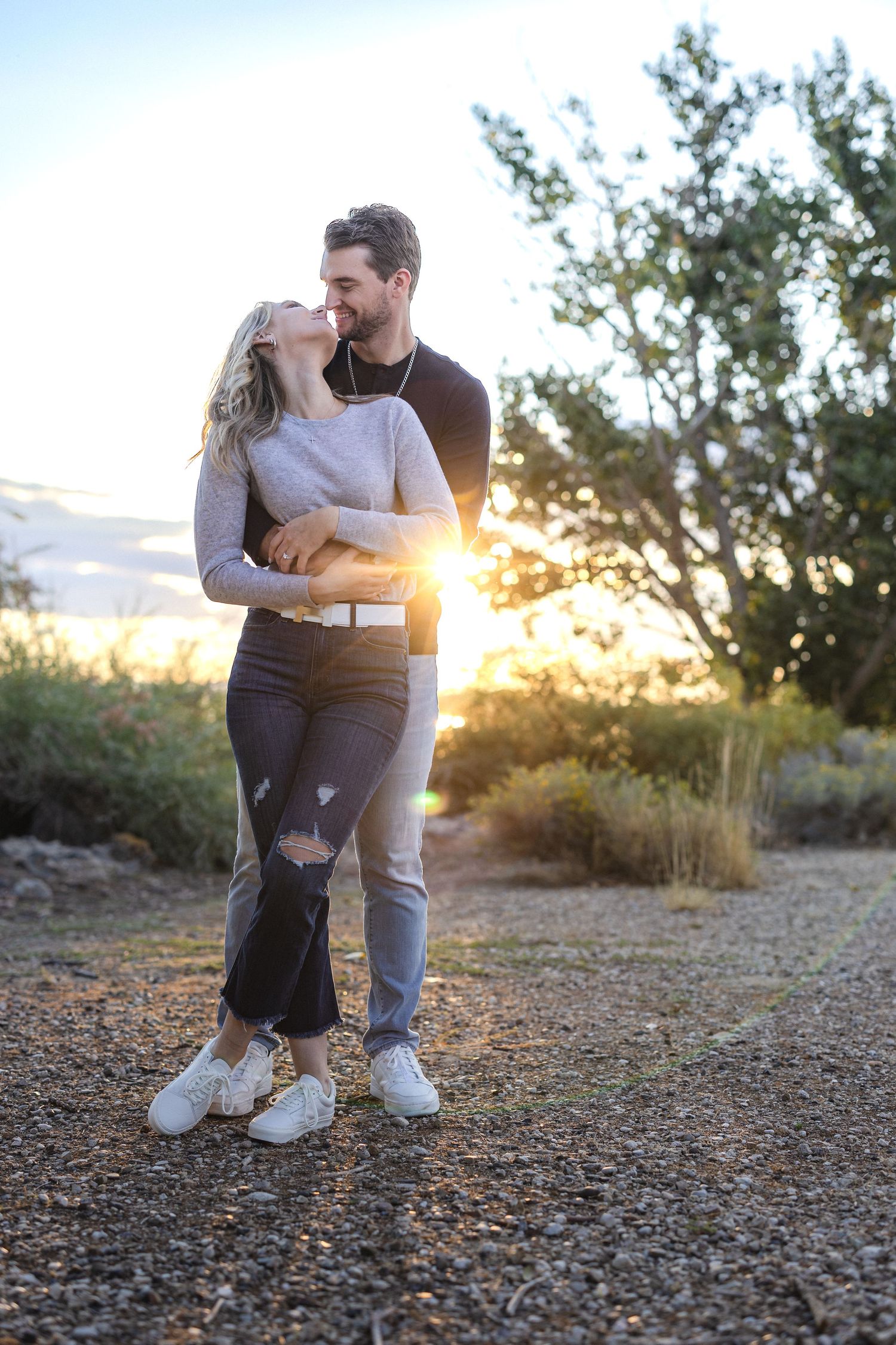 Couple sharing intimate moment at sunset with sunburst between them on dirt path.