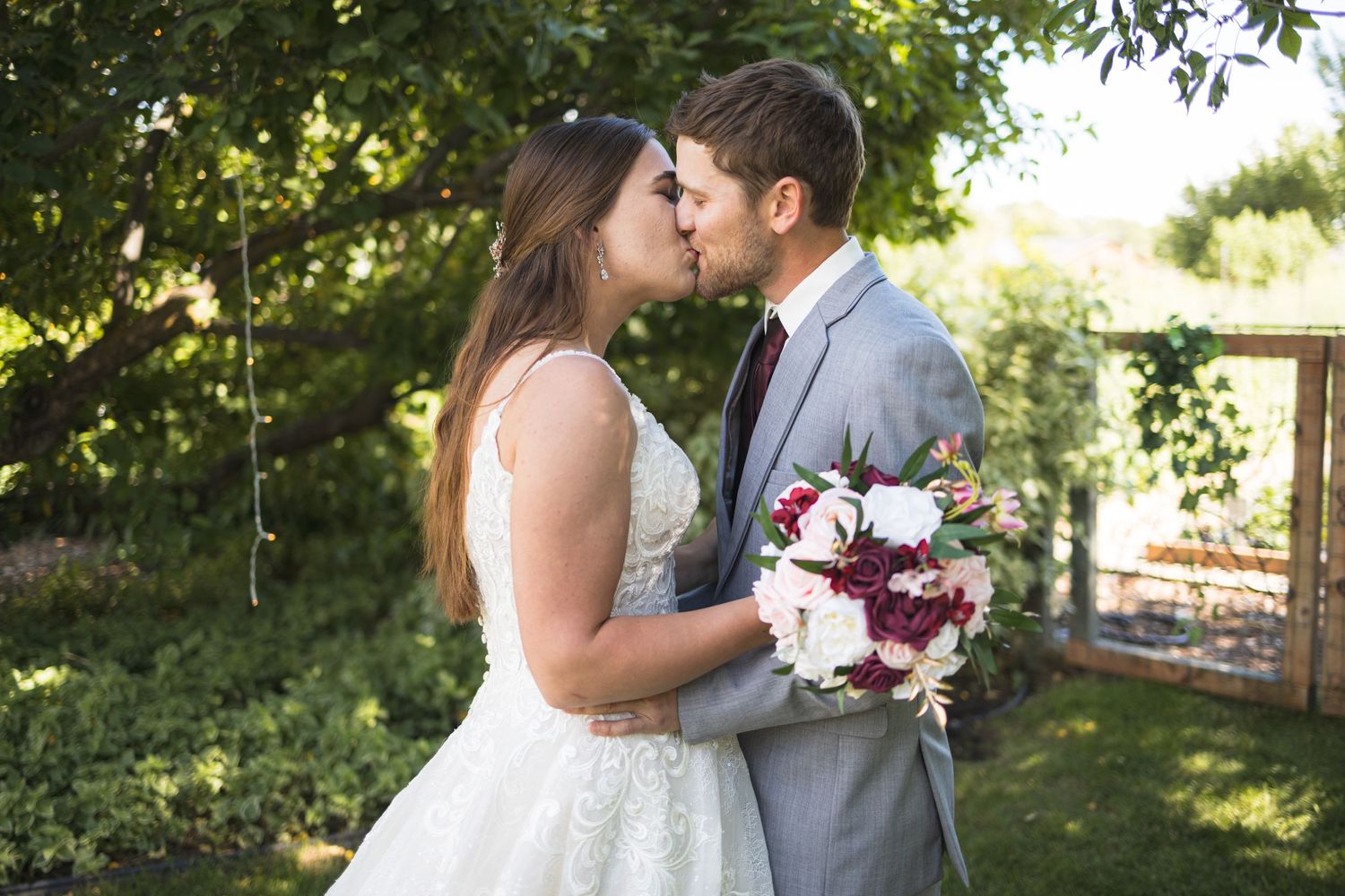 A wedding couple sharing an intimate moment in a garden with burgundy bouquet.