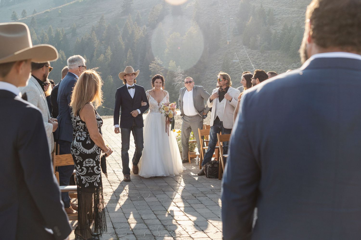 Outdoor mountain wedding ceremony with guests seated in wooden chairs against a dramatic mountain backdrop.