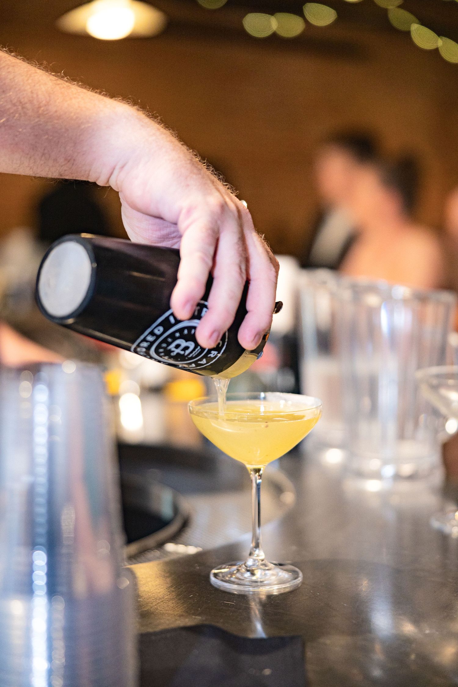 Bartender pouring a yellow cocktail into a martini glass at an elegant bar setting.