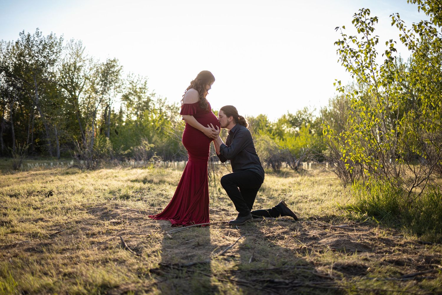 Couple sitting together on a grassy hillside surrounded by nature at sunset.