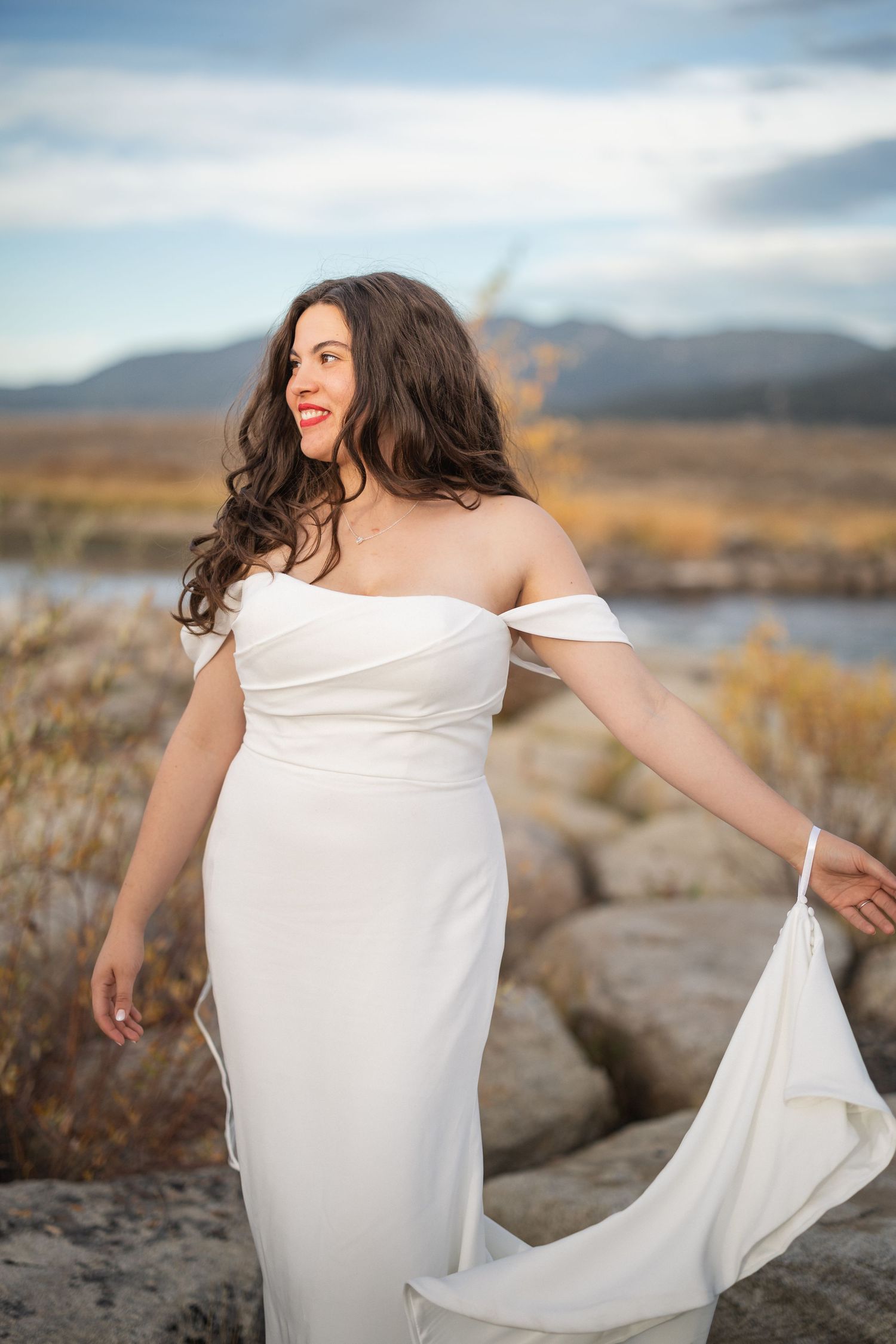 Person in white dress twirling on rocky terrain with mountains and lake in background.