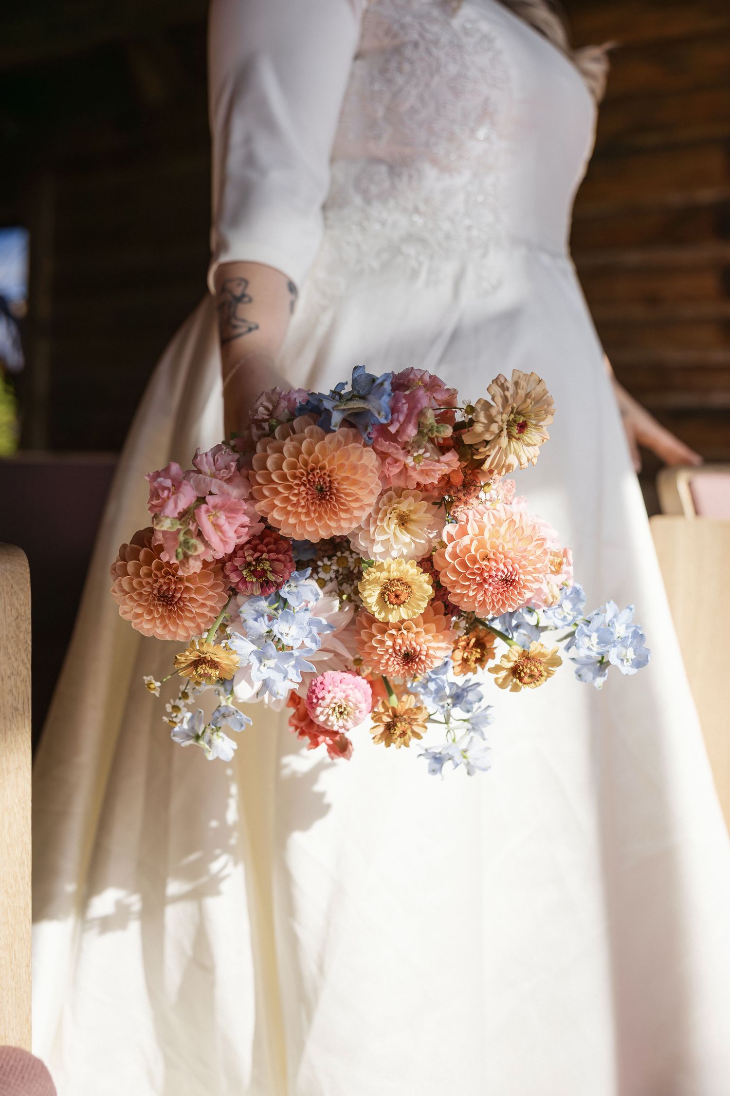 Delicate floral arrangement with peach dahlias and blue flowers adorning a white wedding dress.