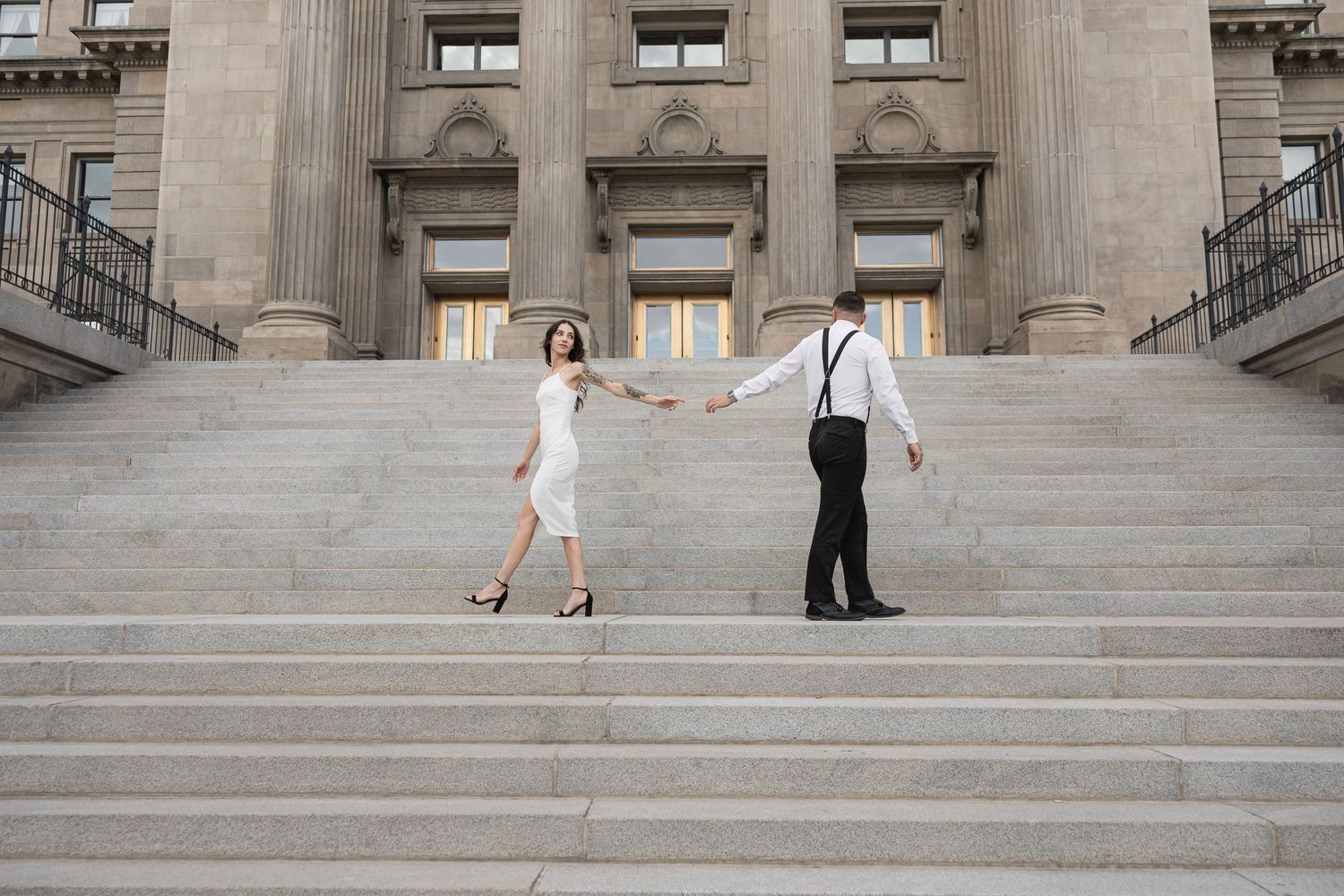 Two people pose on wide stone steps outside a neoclassical building with columns.
