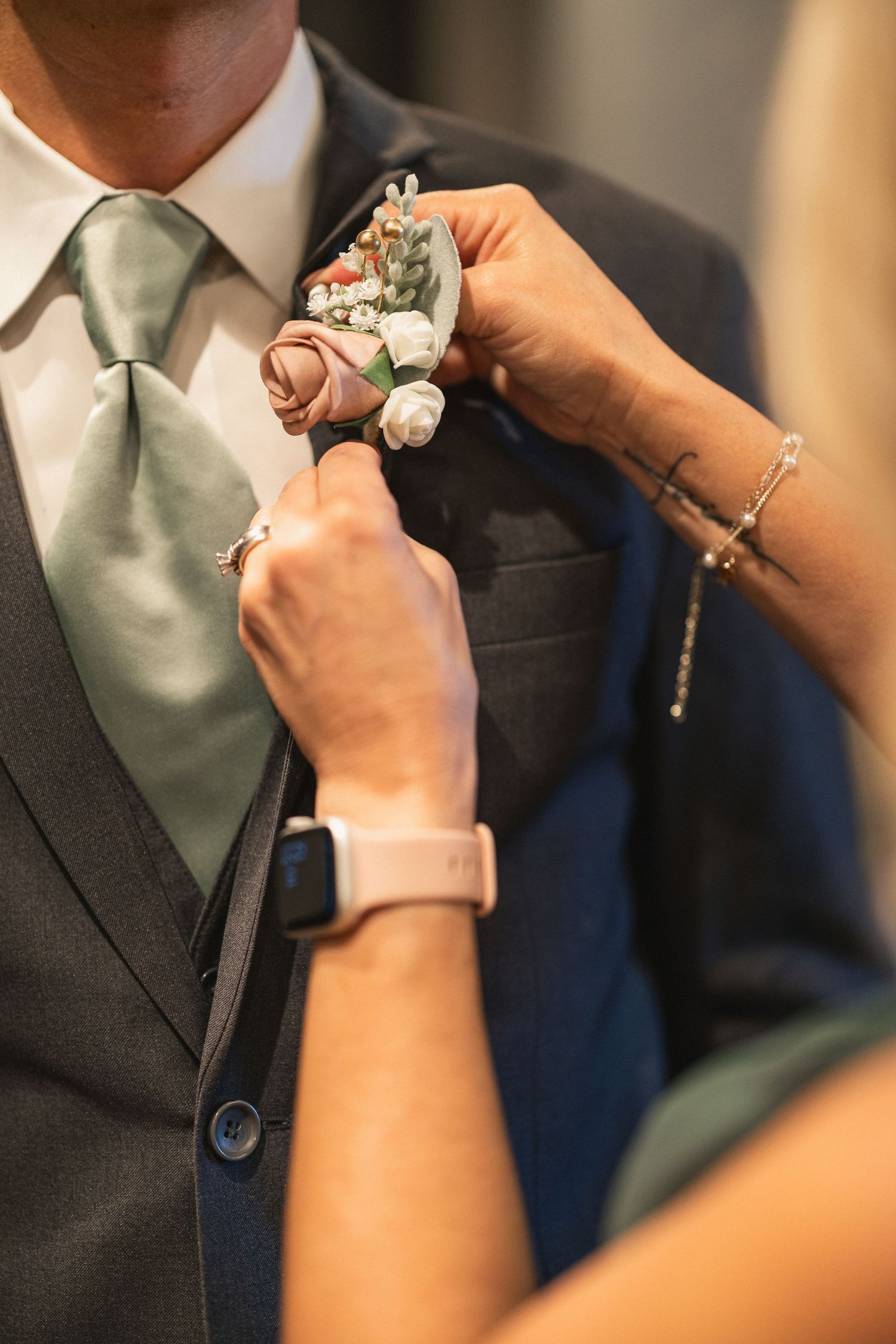 Hands pinning a delicate floral boutonniere onto a dark suit lapel.