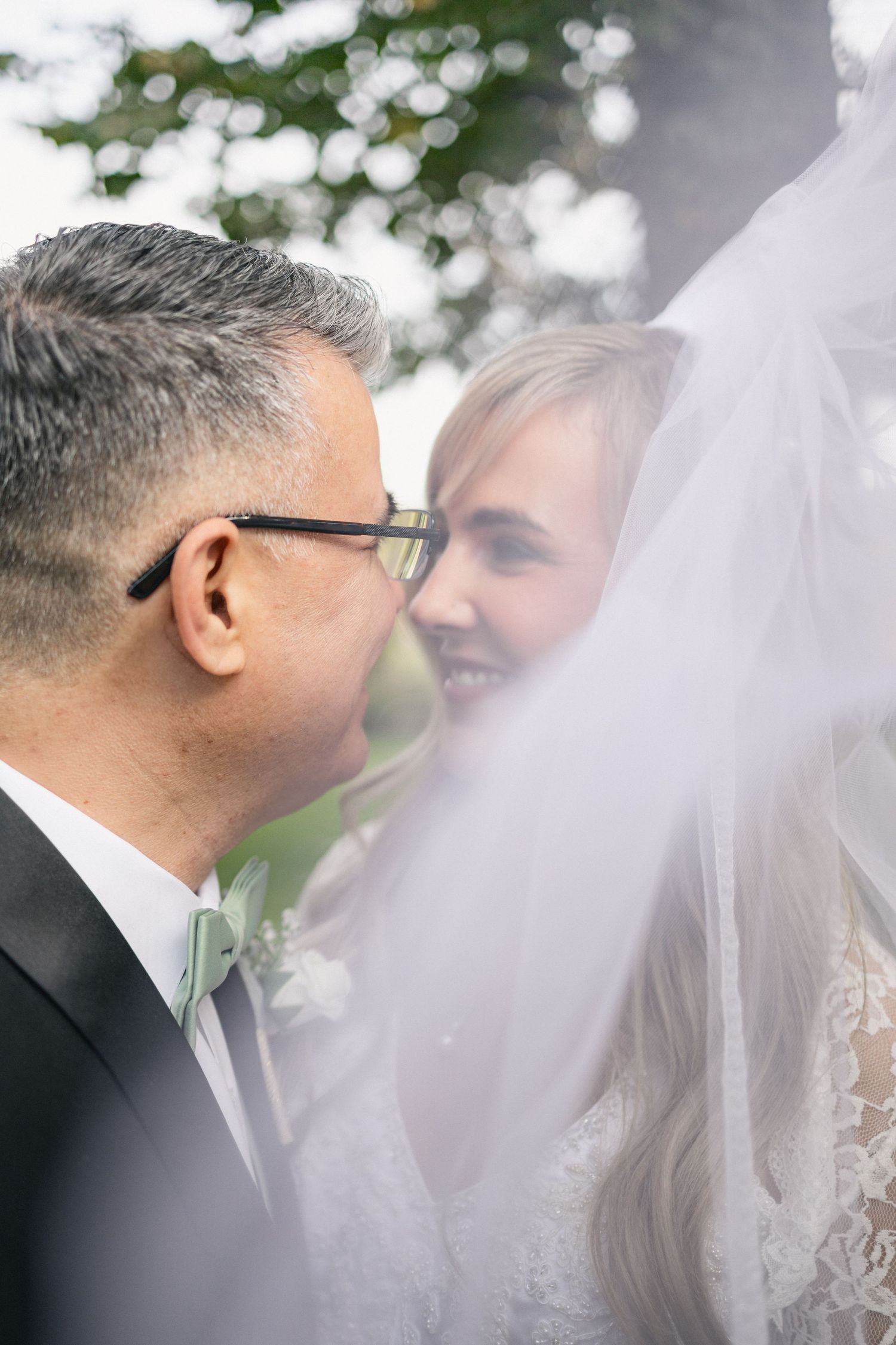 Close-up intimate wedding portrait of couple with veil and glasses in natural lighting.