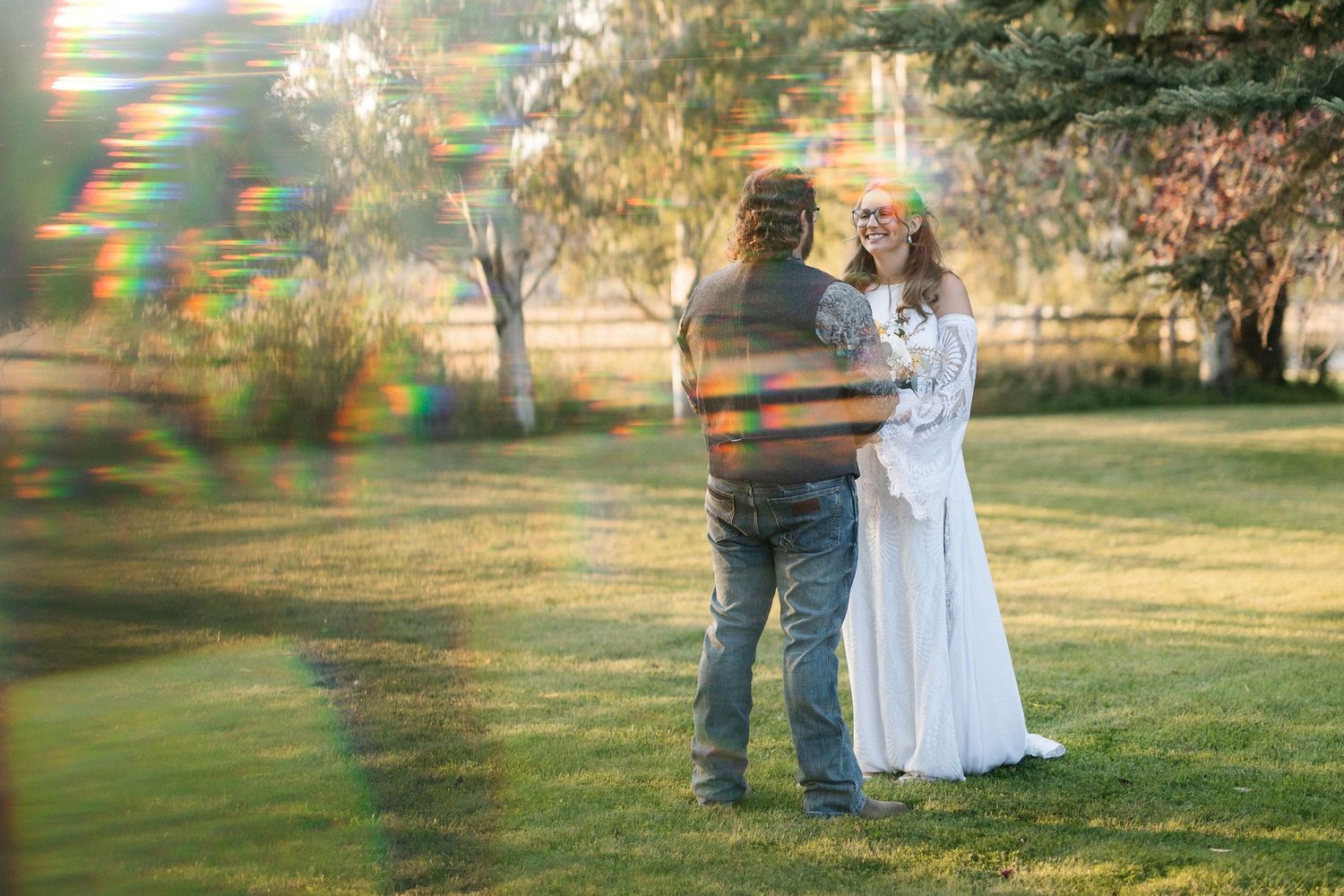 A couple stands together in a sunlit garden with lens flares creating a dreamy atmosphere.