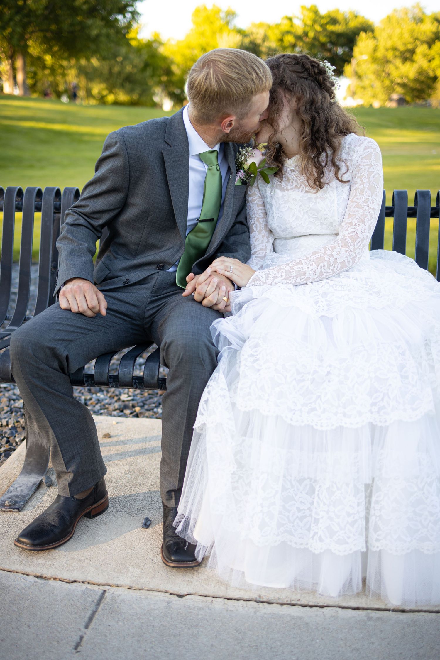 Intimate moment between newlyweds sitting close together on park bench in evening light.