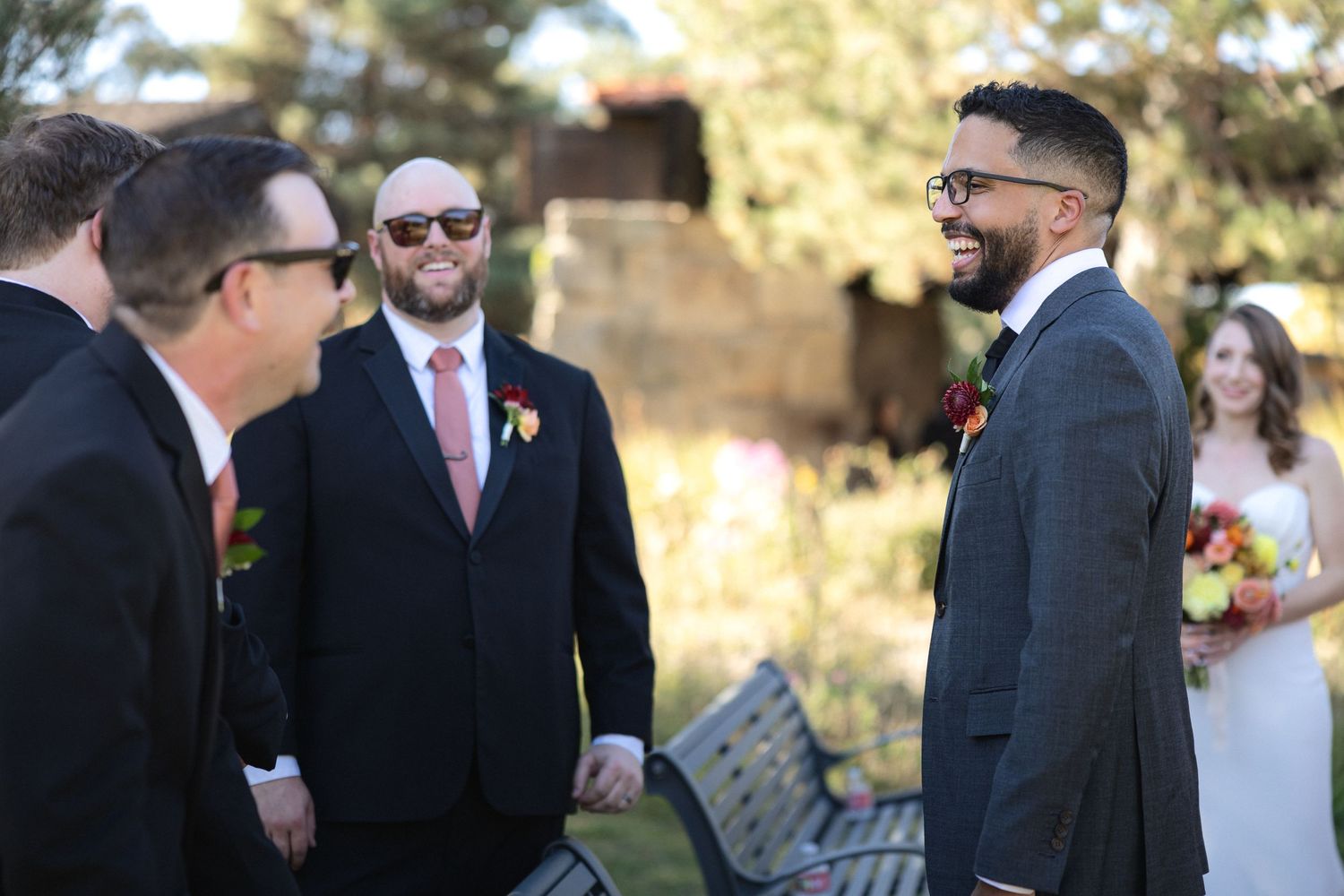 Wedding party gathered during outdoor ceremony with suits and formal attire.