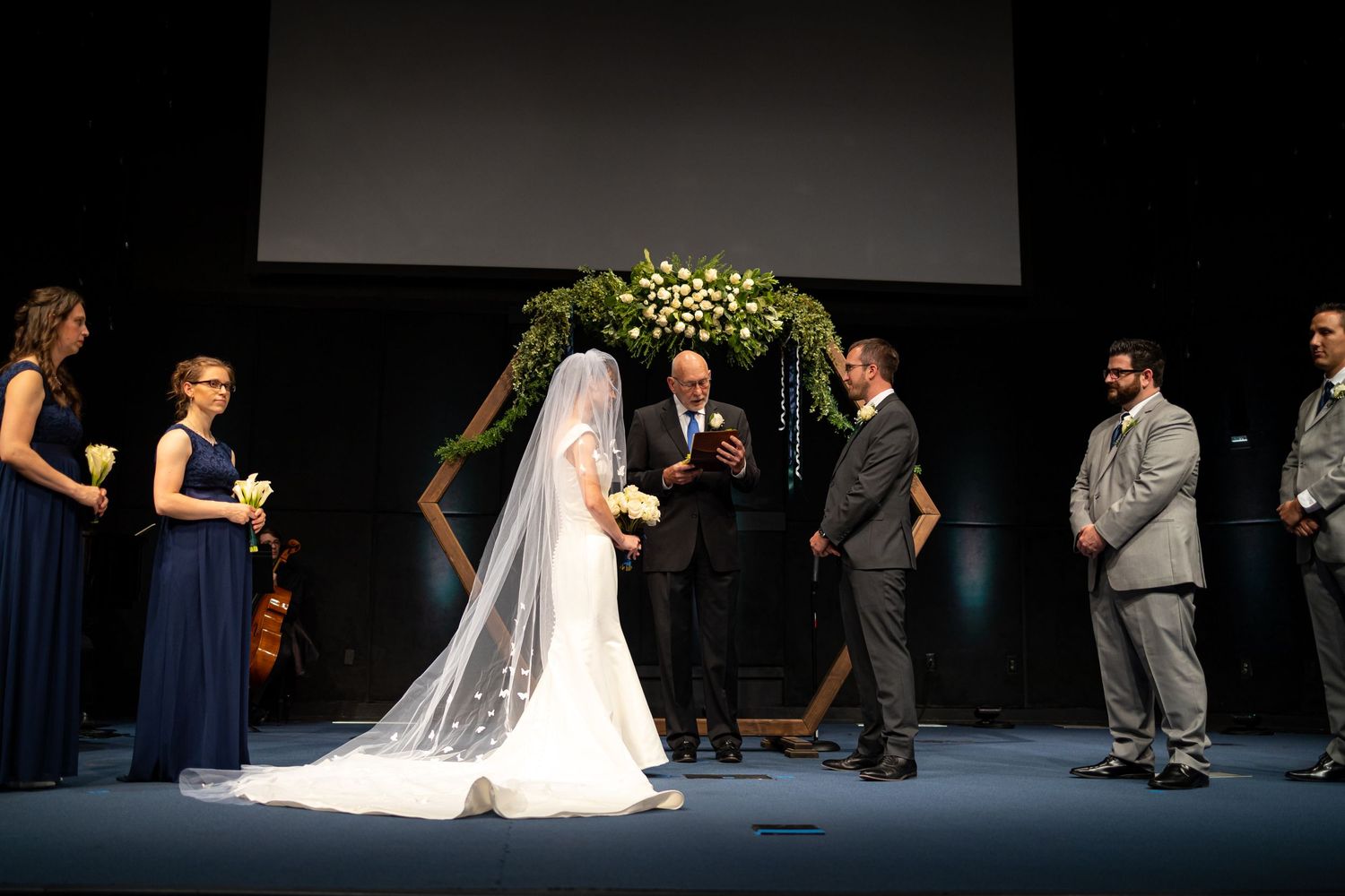 Dramatic stage lighting illuminates a wedding ceremony with dark background.