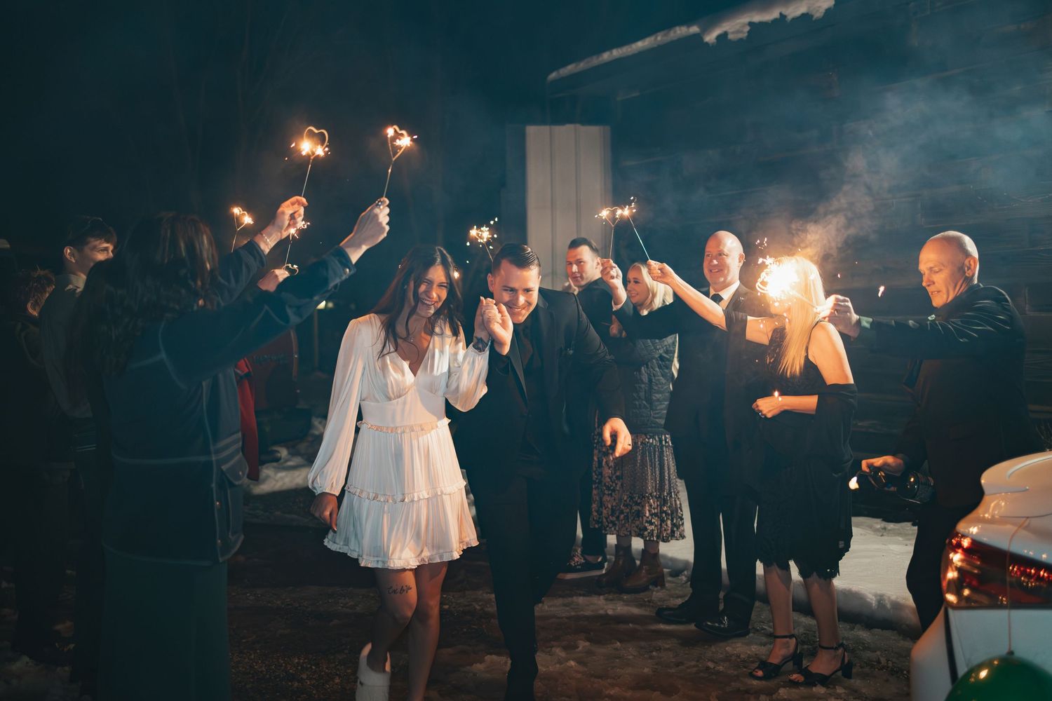 Couple celebrates at night surrounded by guests holding sparklers during wedding festivities.