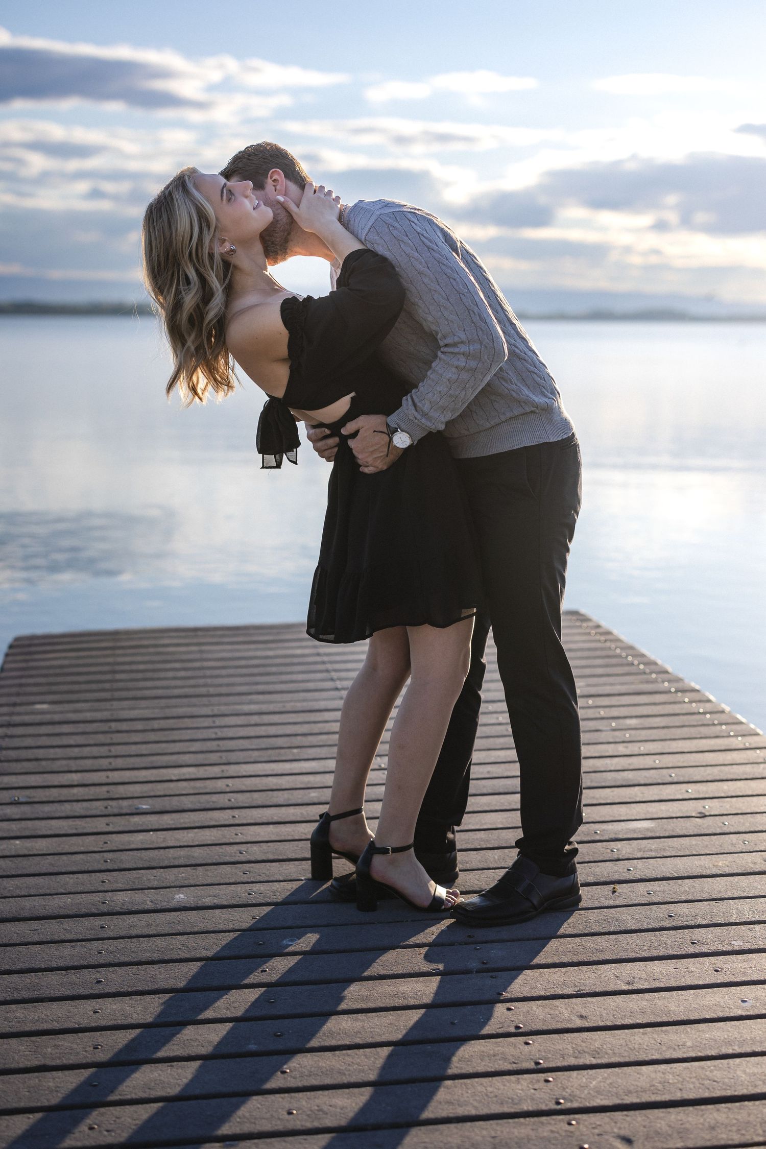 Romantic kiss between couple on wooden dock with sunset lake view.