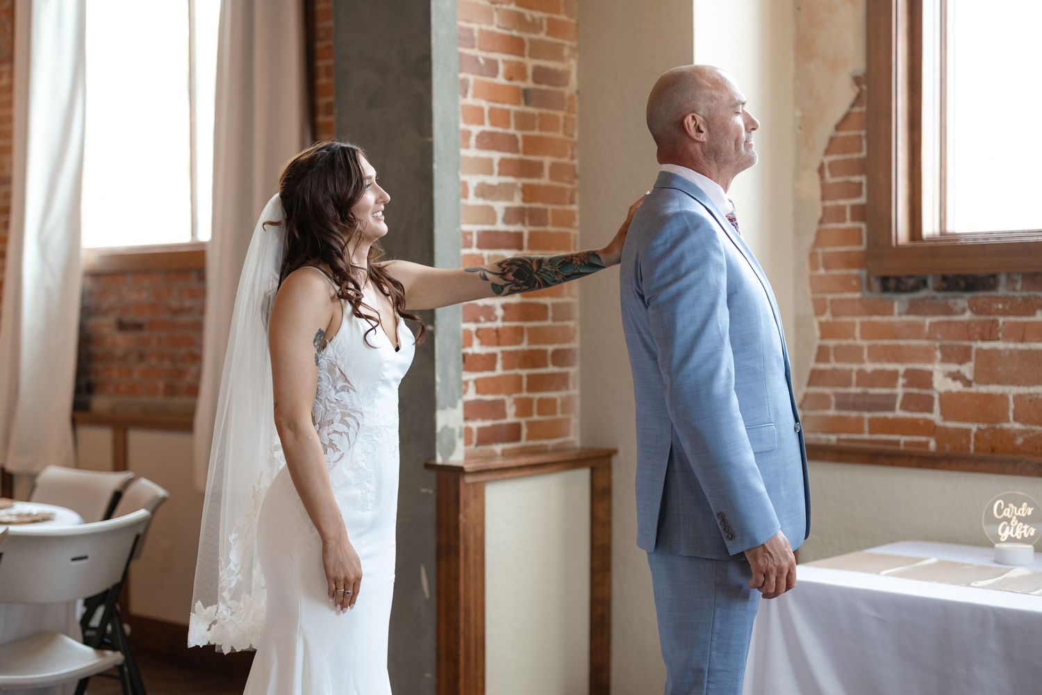 First look moment between couple in elegant wedding attire against brick wall backdrop.