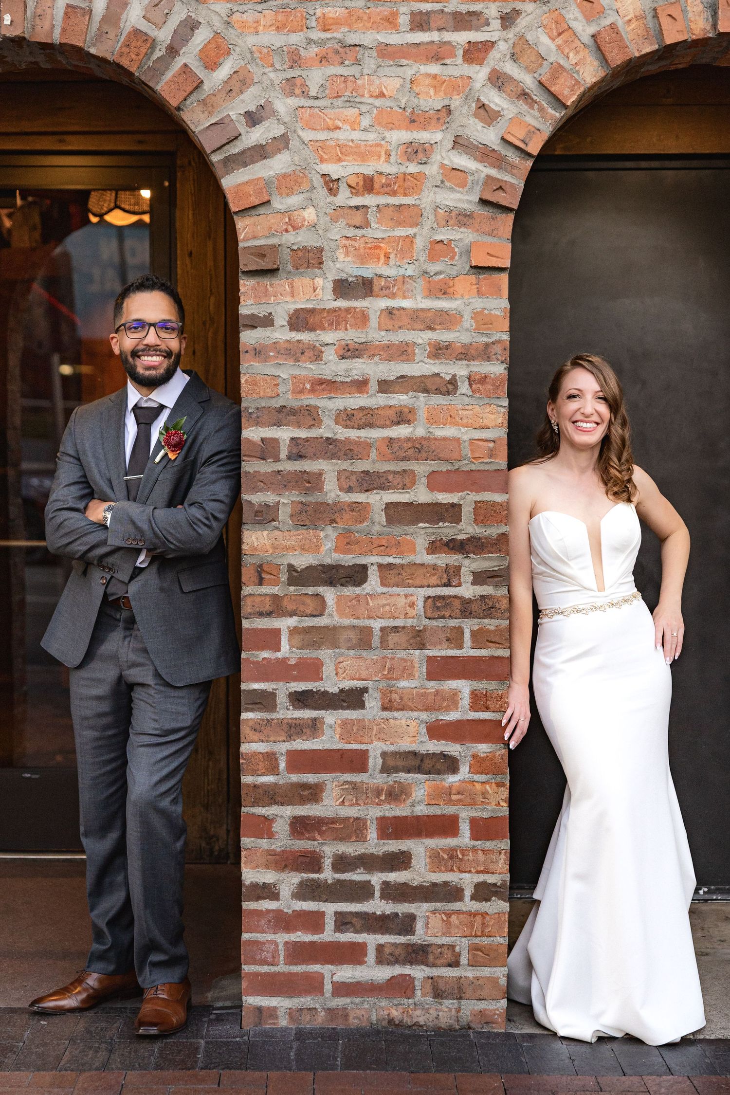 Wedding couple poses separately in adjacent brick archways for creative portrait.