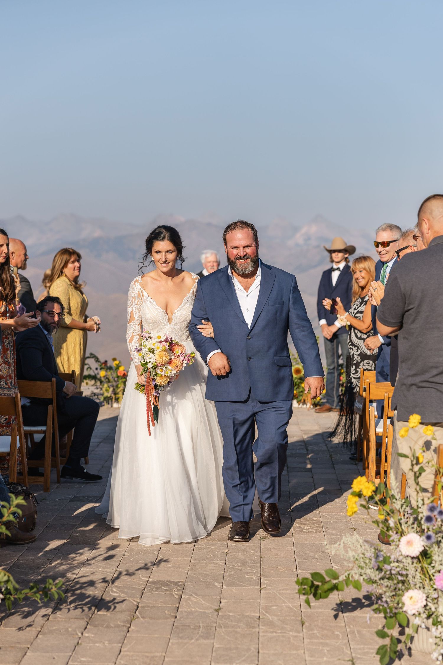 Wedding ceremony guests seated on wooden chairs with mountain vistas in the background.
