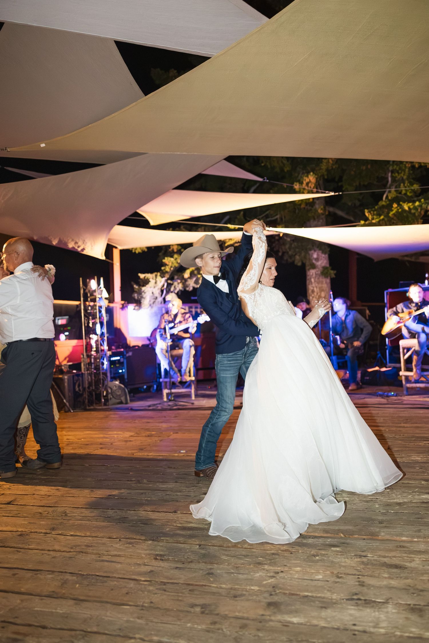 Wedding reception dance floor with flowing white dresses and couples dancing under tent lighting.