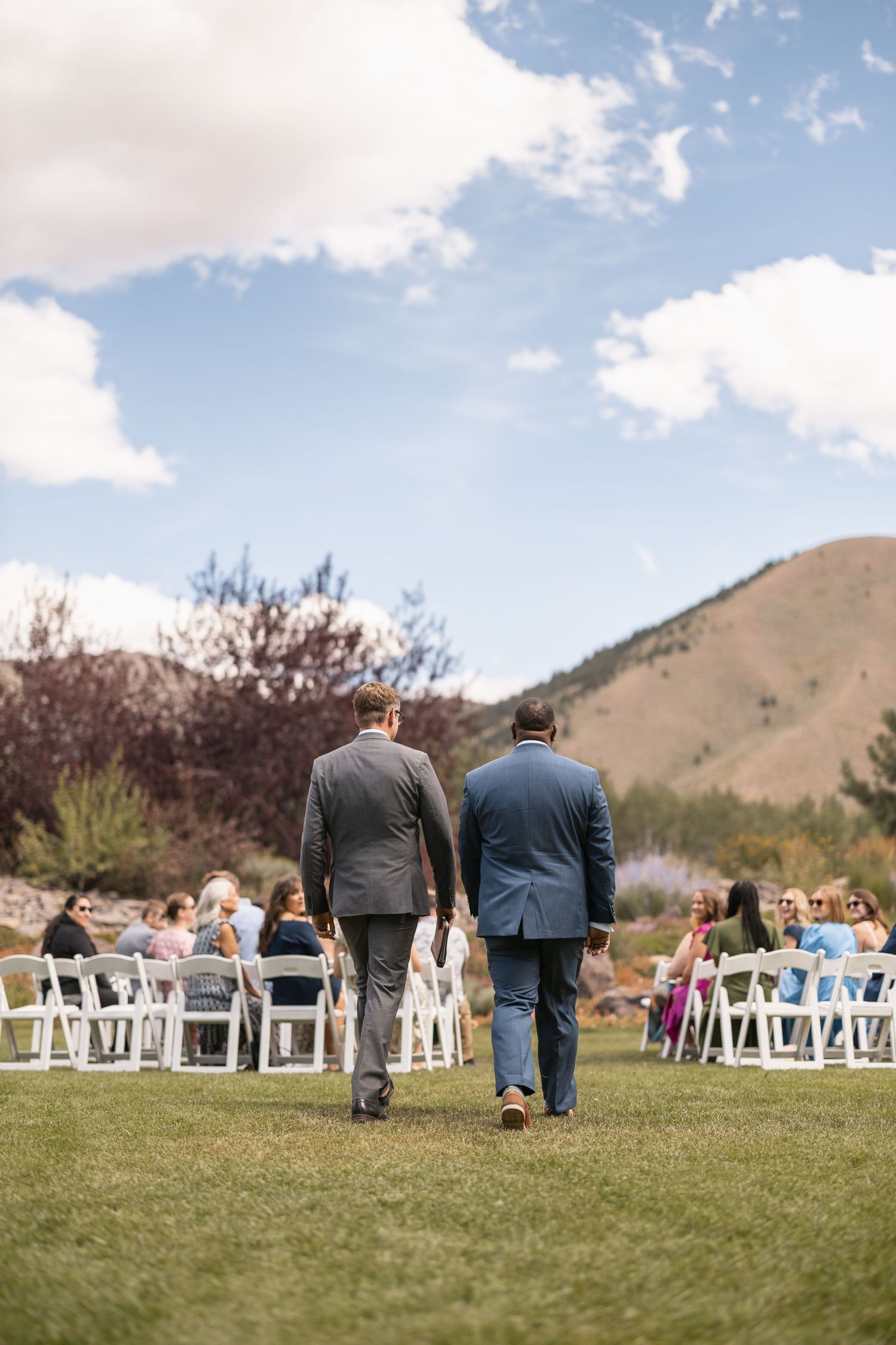 White chairs set up on lawn for outdoor wedding ceremony with mountains in background.