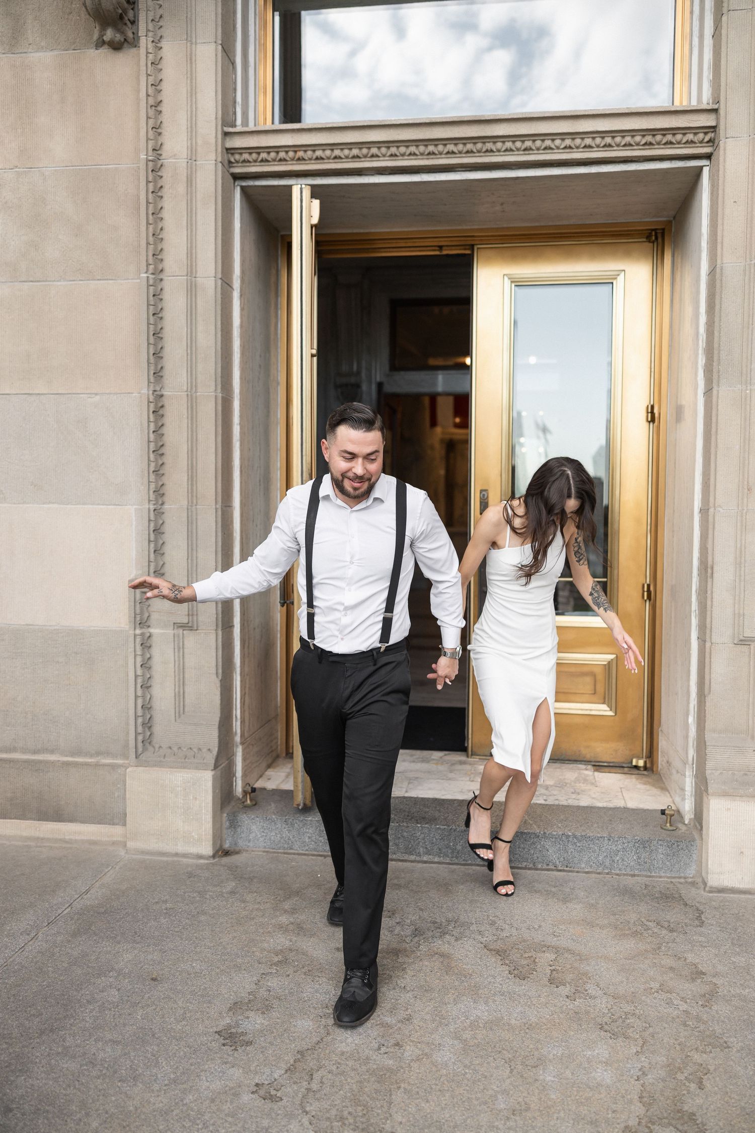 A couple exits through ornate golden doors of a historic building.