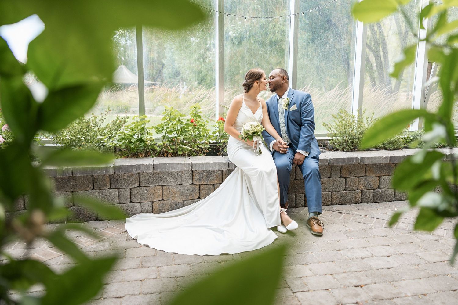 Wedding photography session in a lush green garden setting with brick wall backdrop.