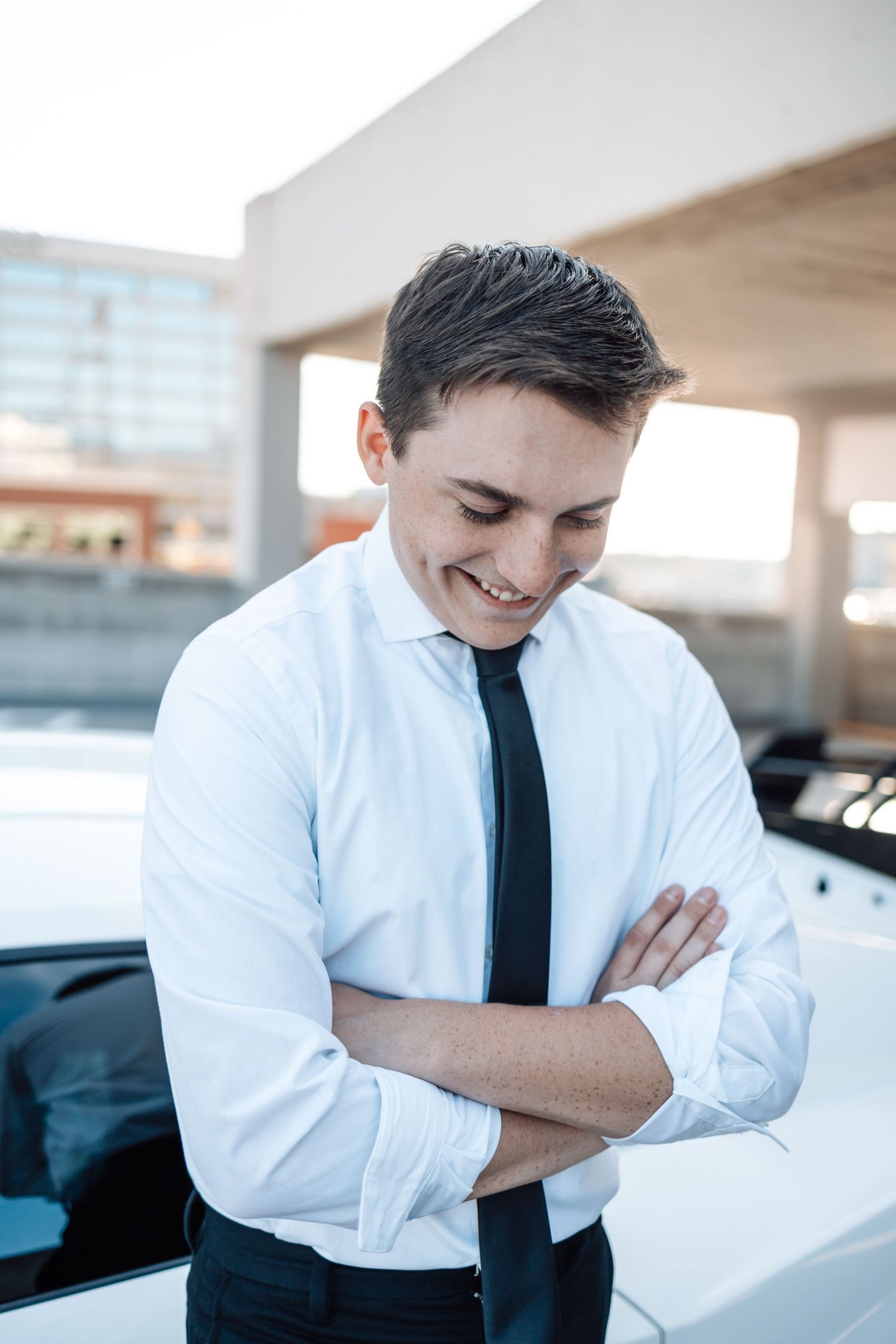 Professional in white dress shirt and black tie stands confidently with arms crossed in bright modern office setting.