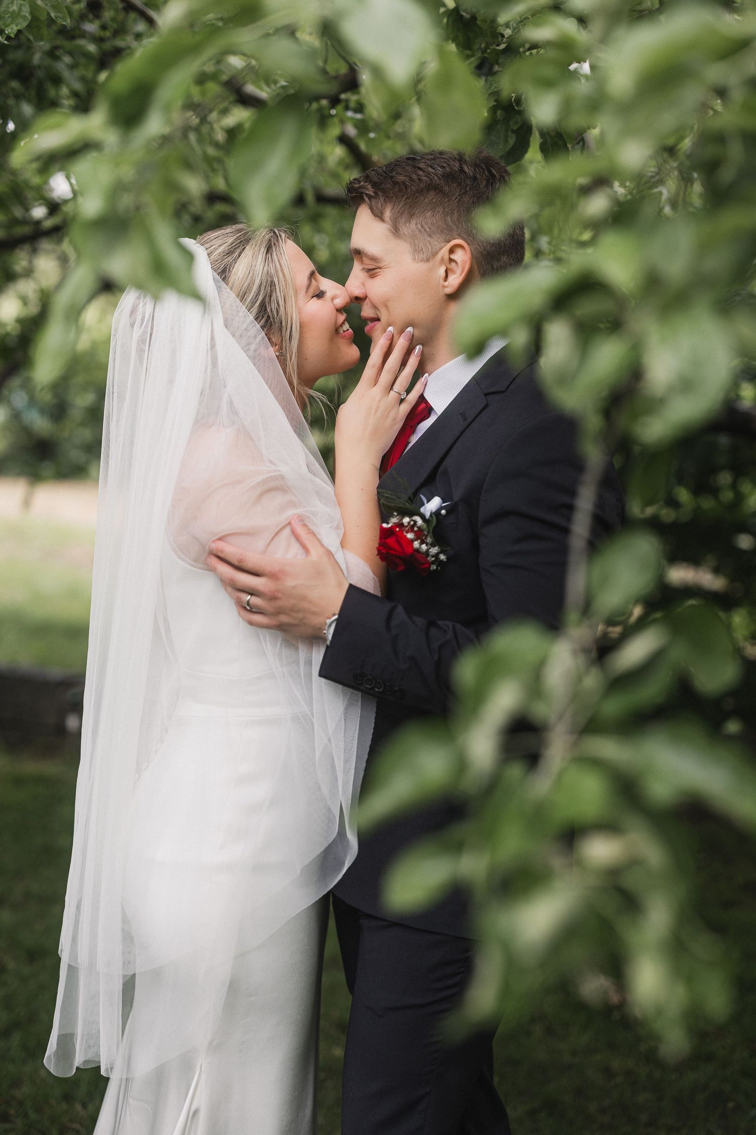 Newlywed couple shares intimate moments in a lush garden setting with flowing white veil and formal attire.