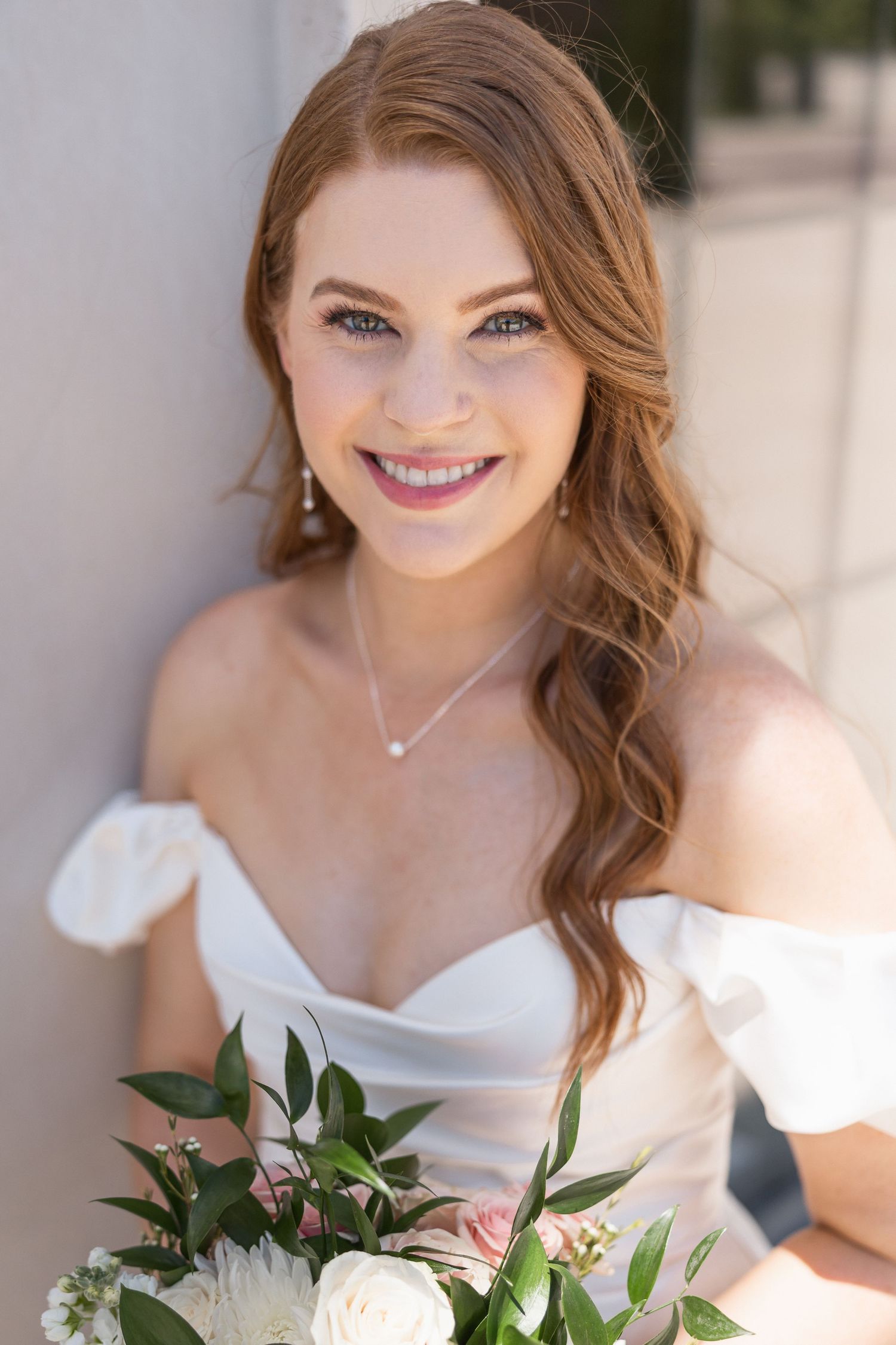 A bridal portrait showing a white dress and bouquet against a light background.