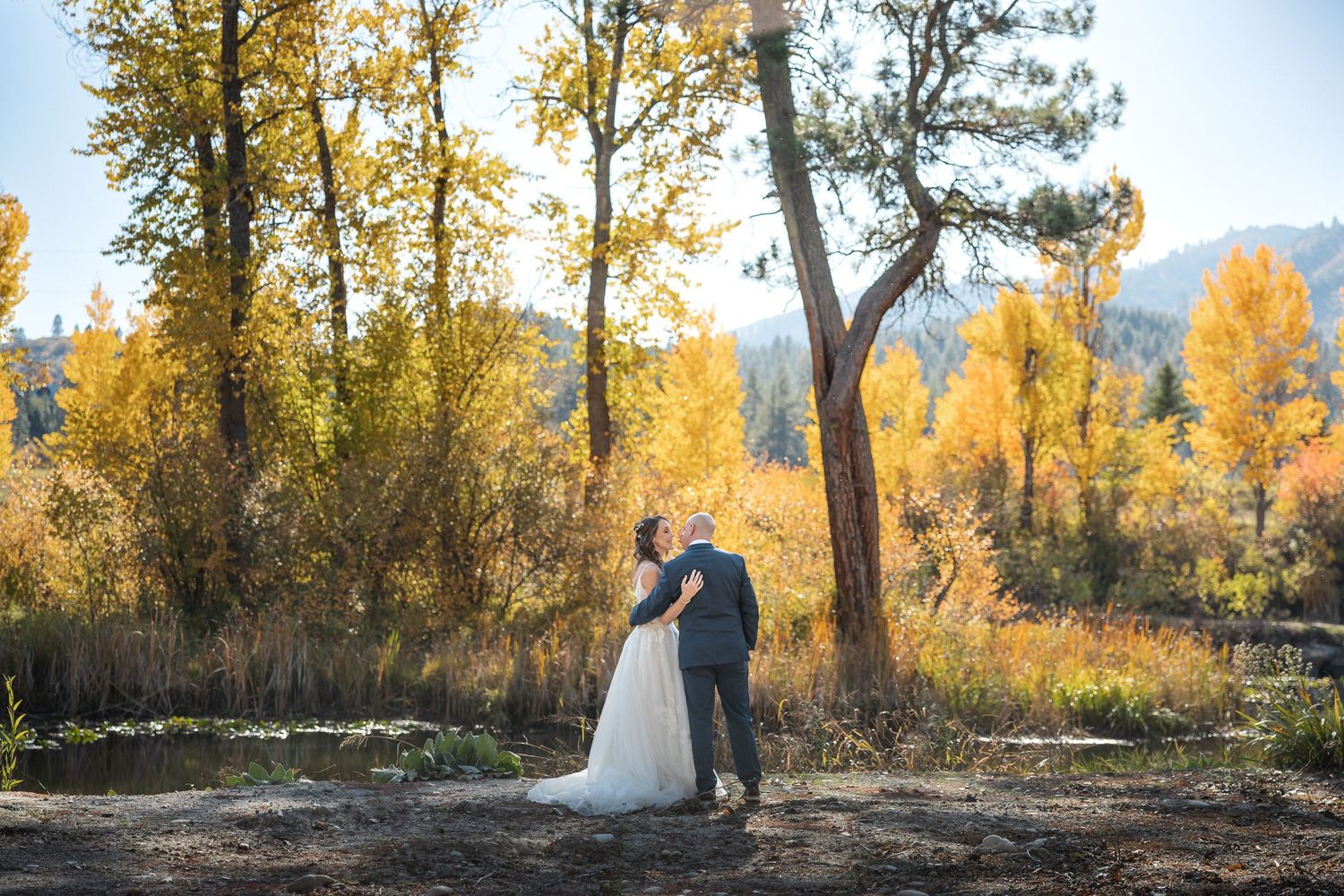 A couple embraces in a romantic autumn setting with golden trees and mountain views in the background.