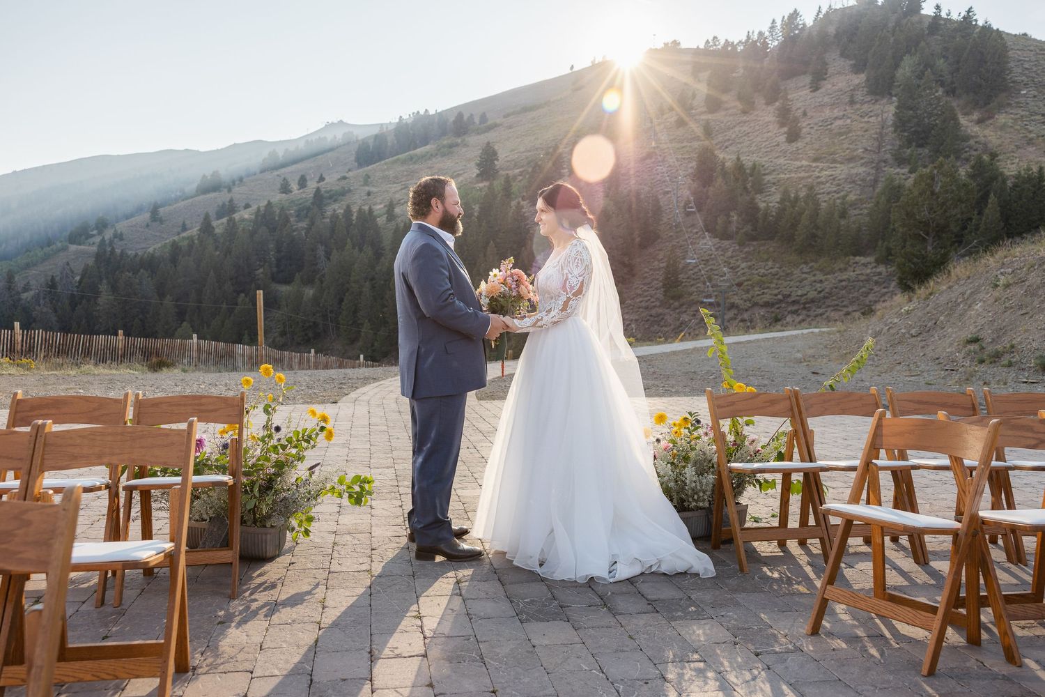 Wedding ceremony setup on stone patio with wooden chairs and mountain vista backdrop.