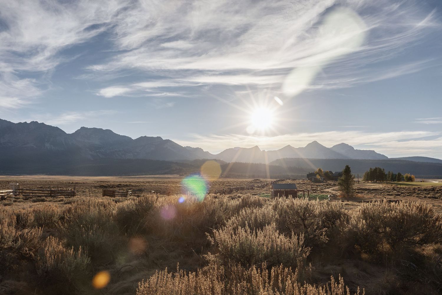 Panoramic view of a desert landscape with mountains and sagebrush under dramatic cloudy skies at sunset.