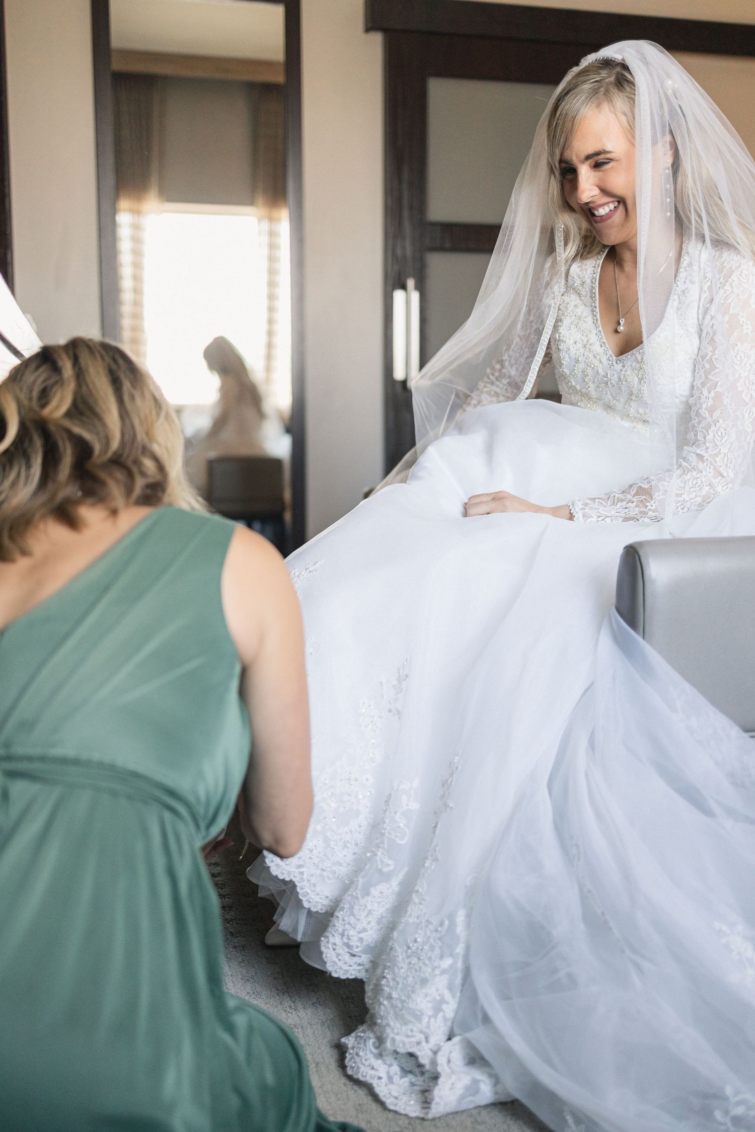 Bridesmaid helping bride with wedding dress details during pre-ceremony preparations.