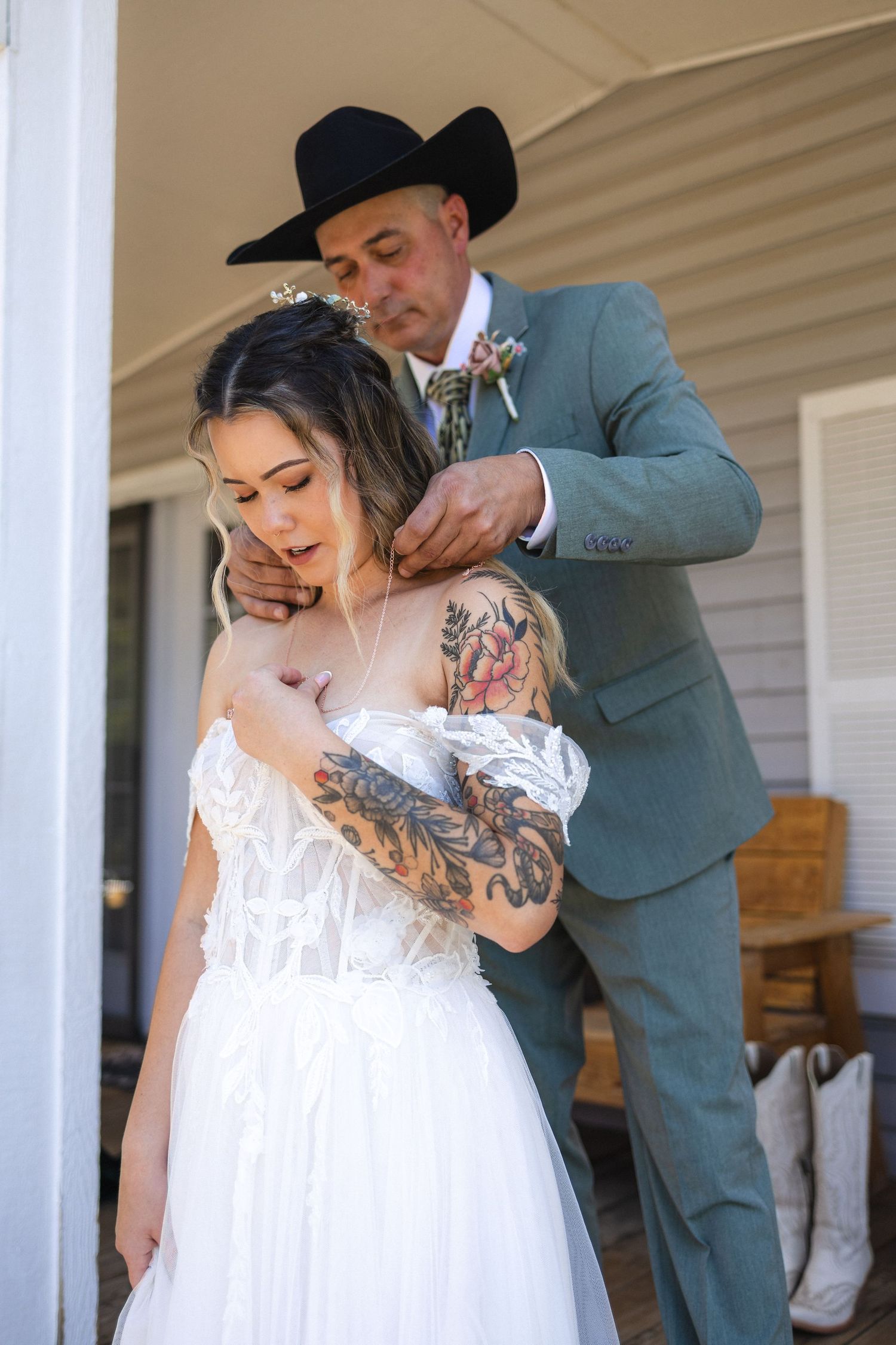 Wedding couple in rustic setting with bride in white dress and groom in sage suit and cowboy hat.