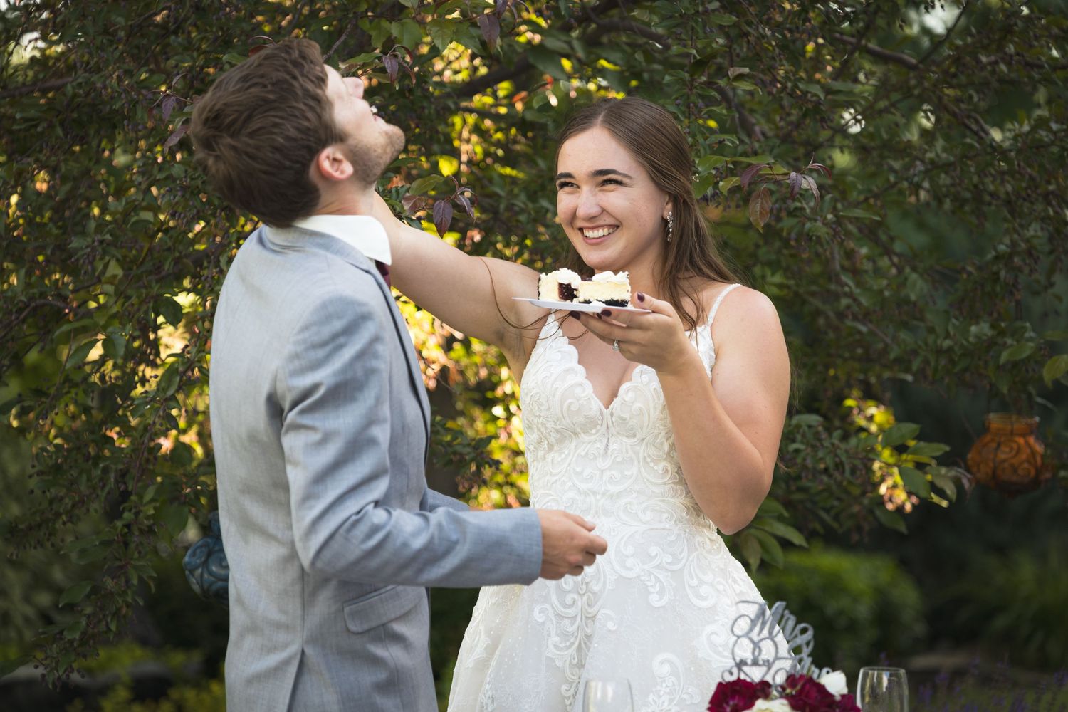 Newlyweds playfully feed each other cake at their outdoor wedding reception.