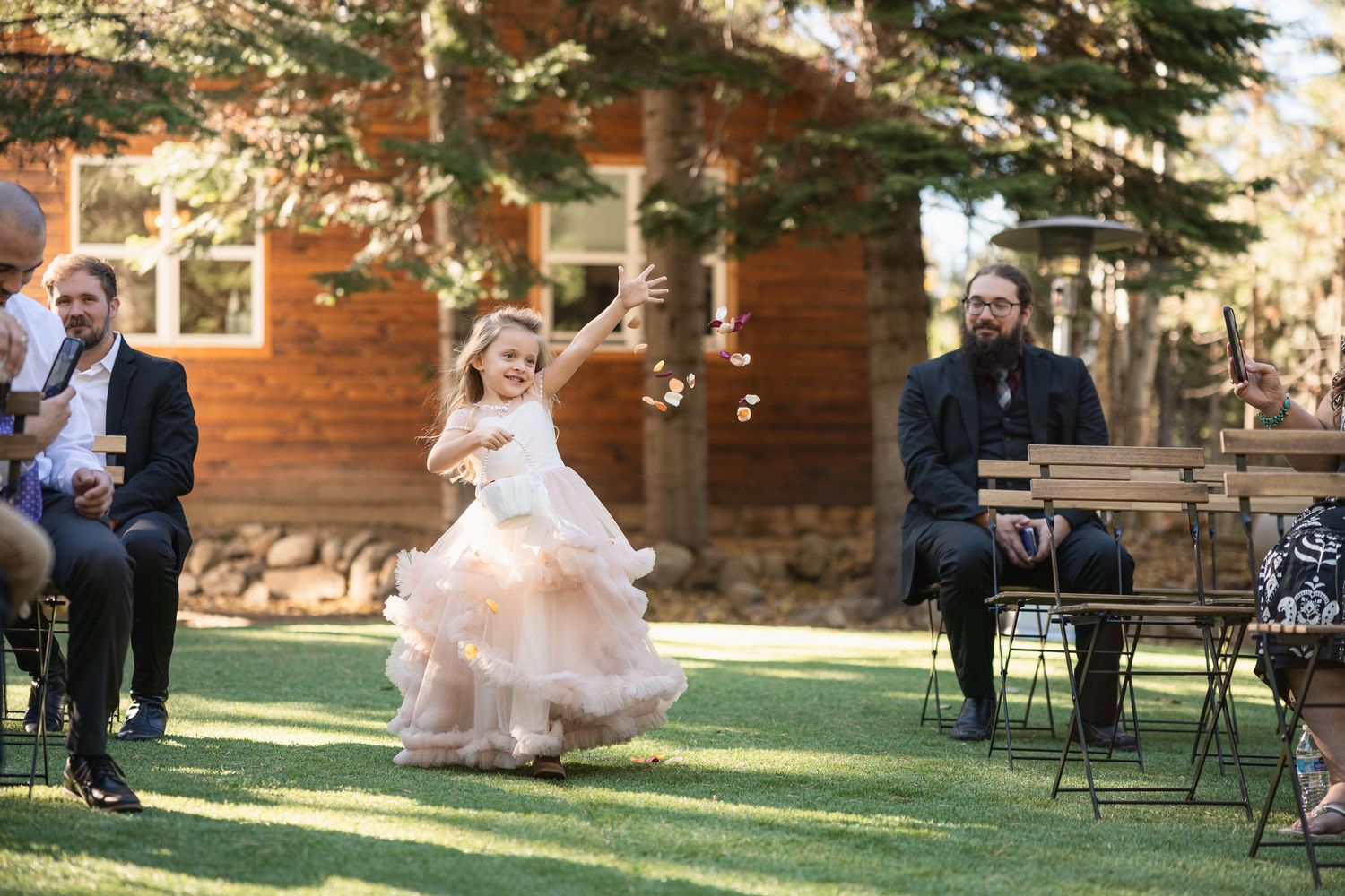 Child in flowing pink dress twirling at outdoor wedding celebration.
