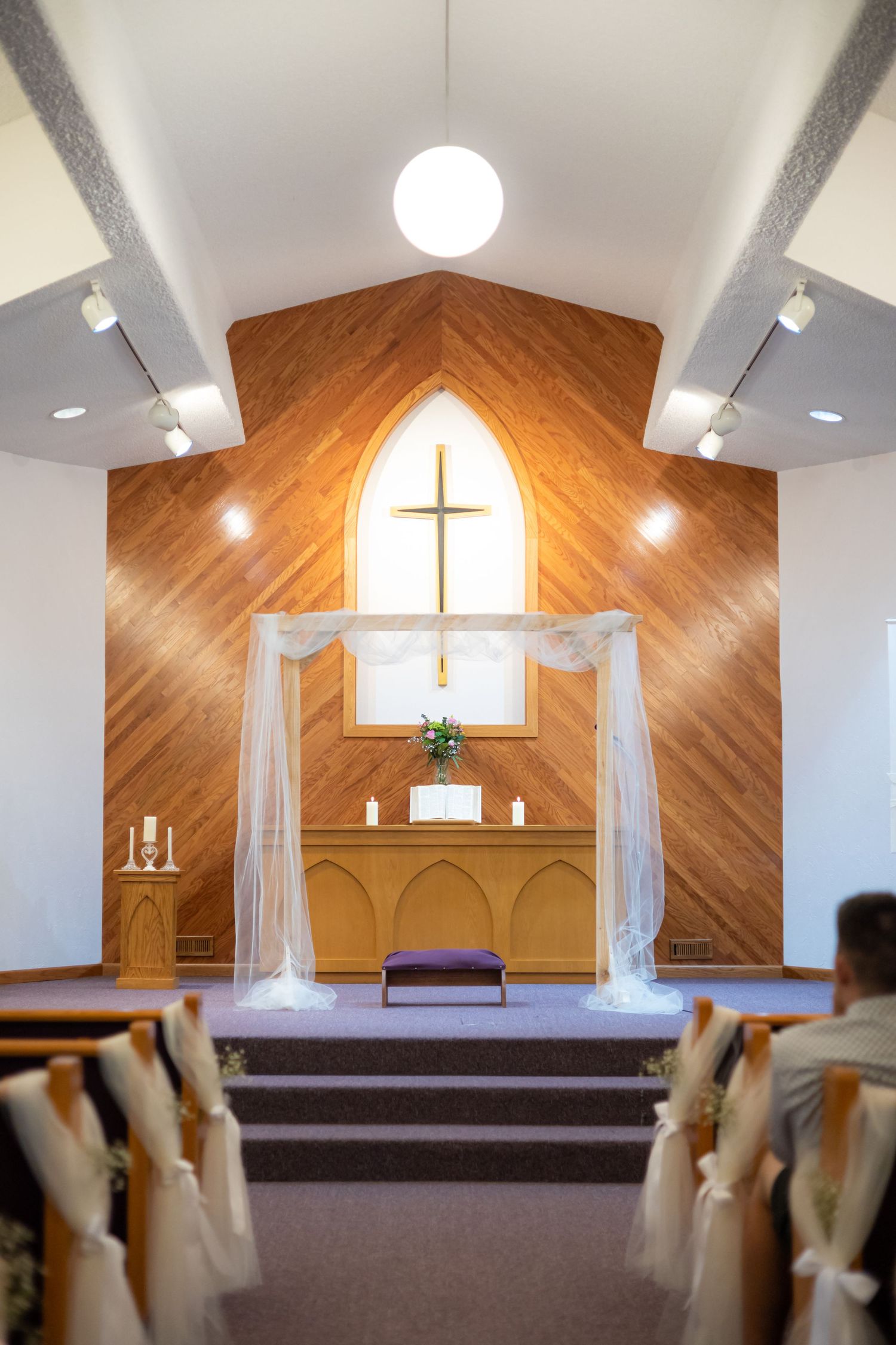 Interior of a church sanctuary with wooden paneled walls and a cross illuminated by natural light.
