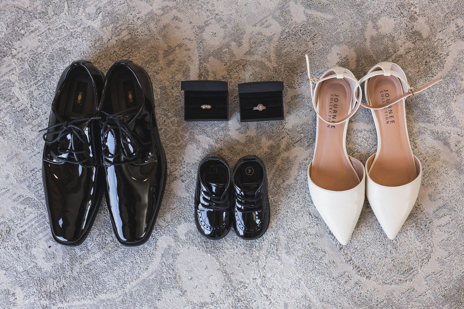 Wedding shoes and ring boxes arranged on grey surface with floral accents.