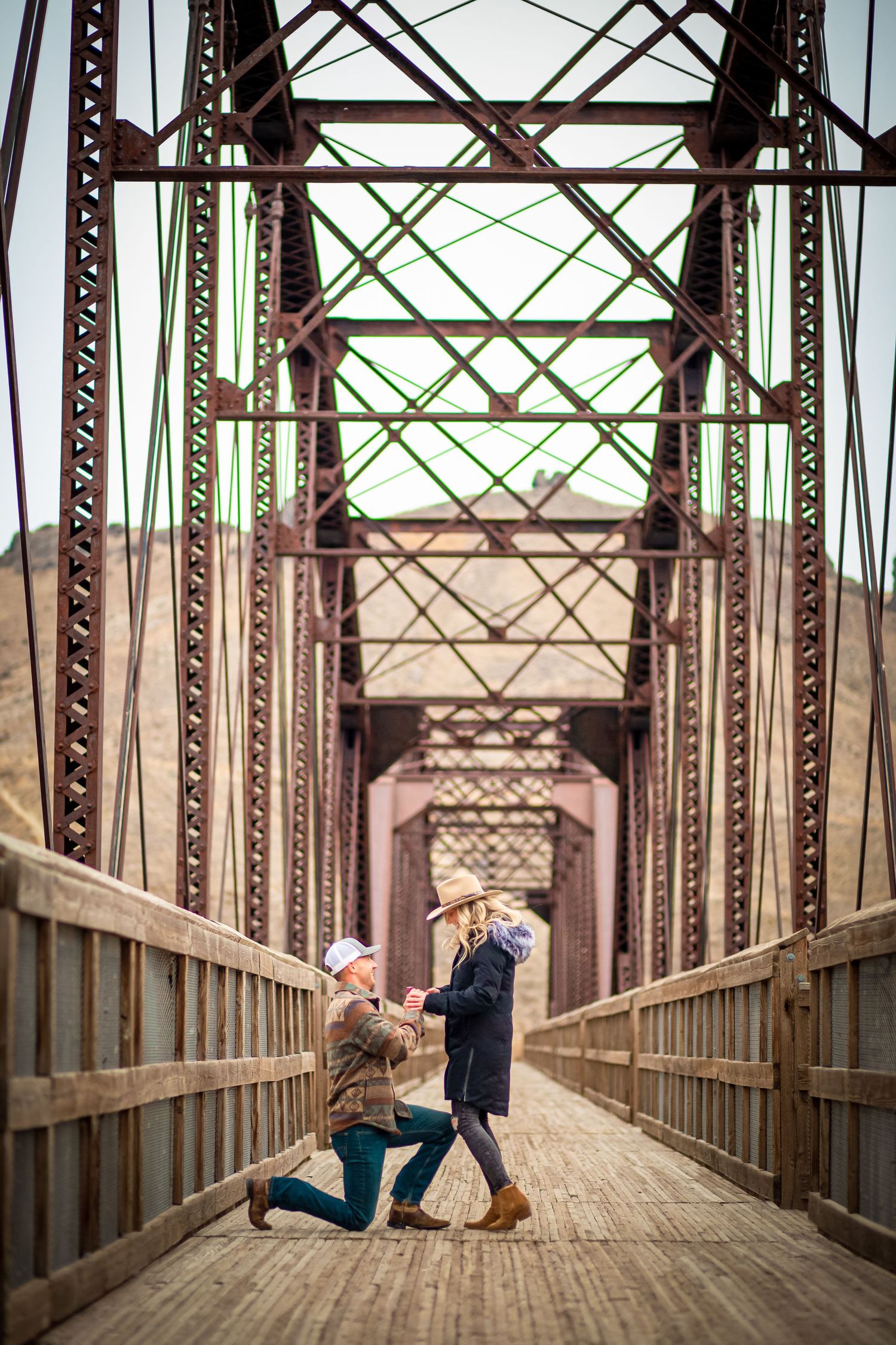 Couple poses on historic metal bridge with industrial architecture in background.