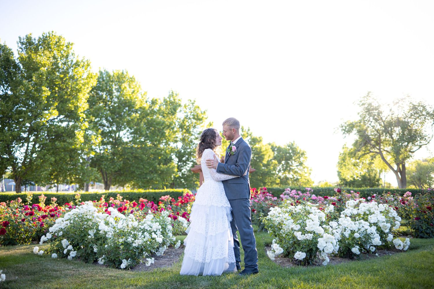 Wedding couple embracing in garden with white and red flowers in background.