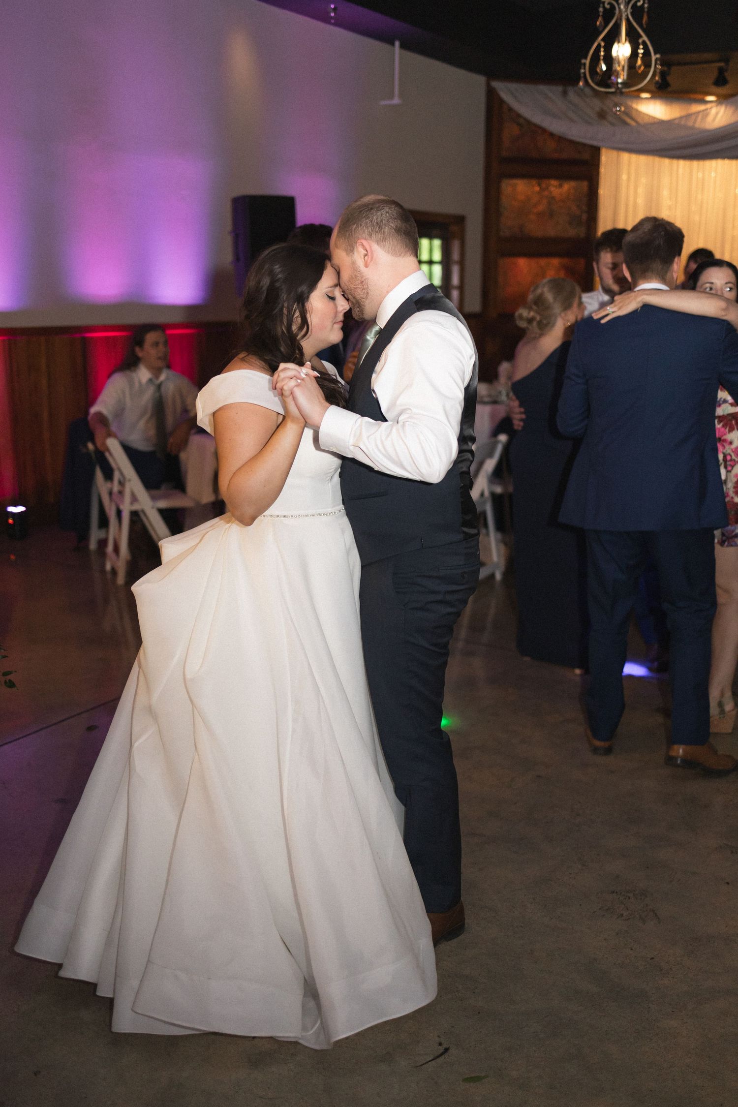 A couple shares a romantic dance at their wedding reception with purple uplighting in the background.