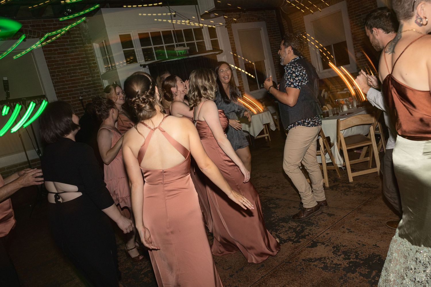 Dance party at wedding reception with colorful lighting in an industrial brick venue.