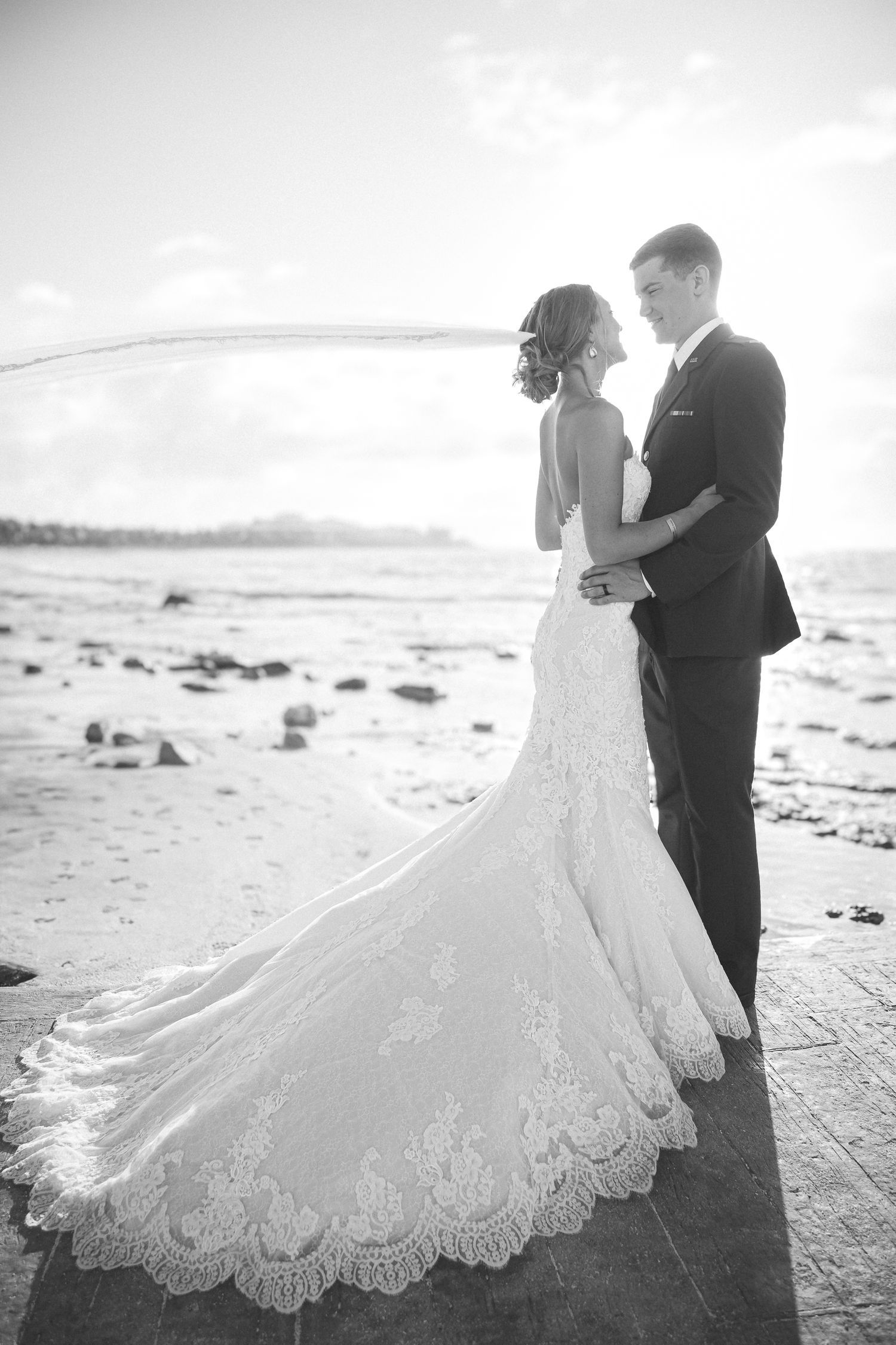 Romantic black and white beach wedding photo with bride in lace train dress at sunset.