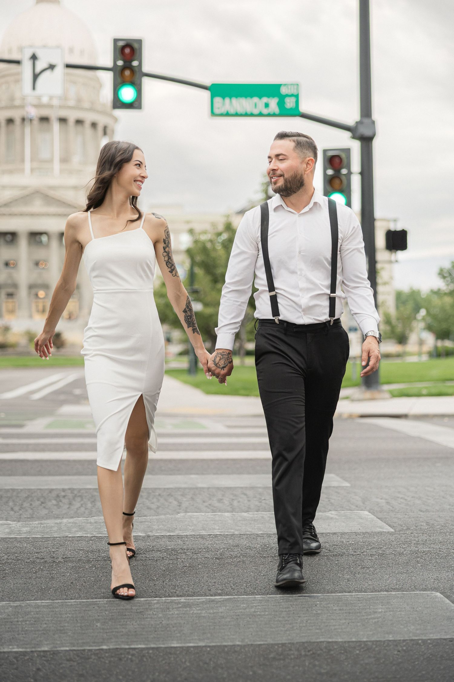 A couple in black and white attire walk together on a city street near traffic signs.