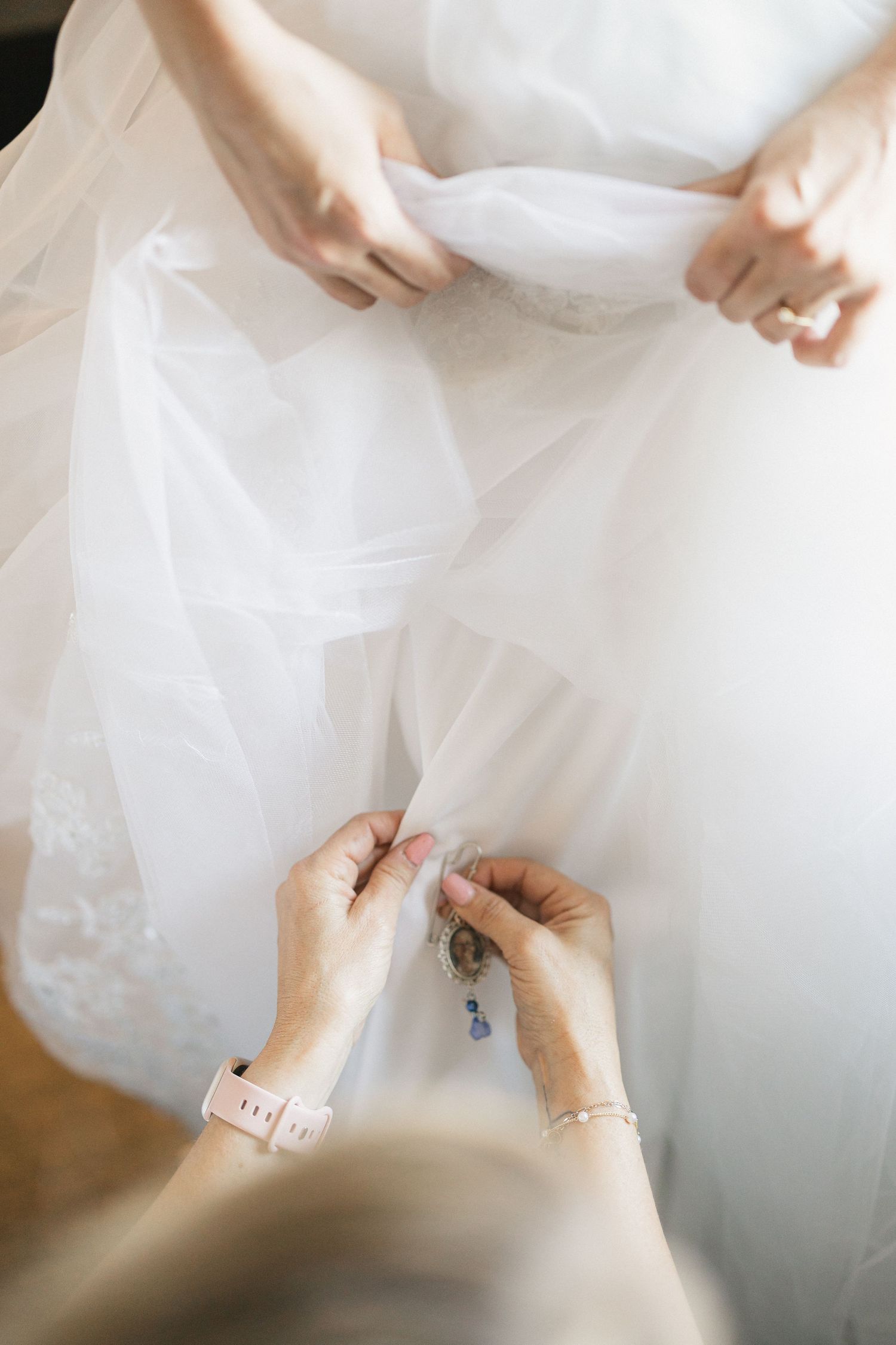 Hands delicately adjusting white tulle fabric of a wedding dress.