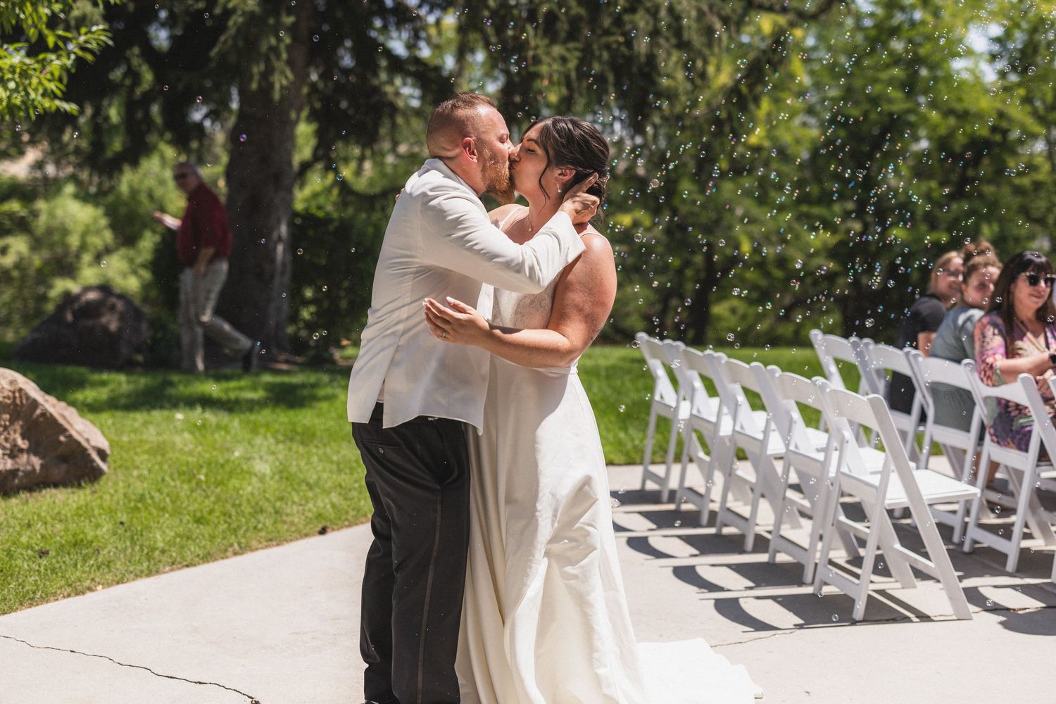Wedding ceremony taking place outdoors with white chairs and natural backdrop.