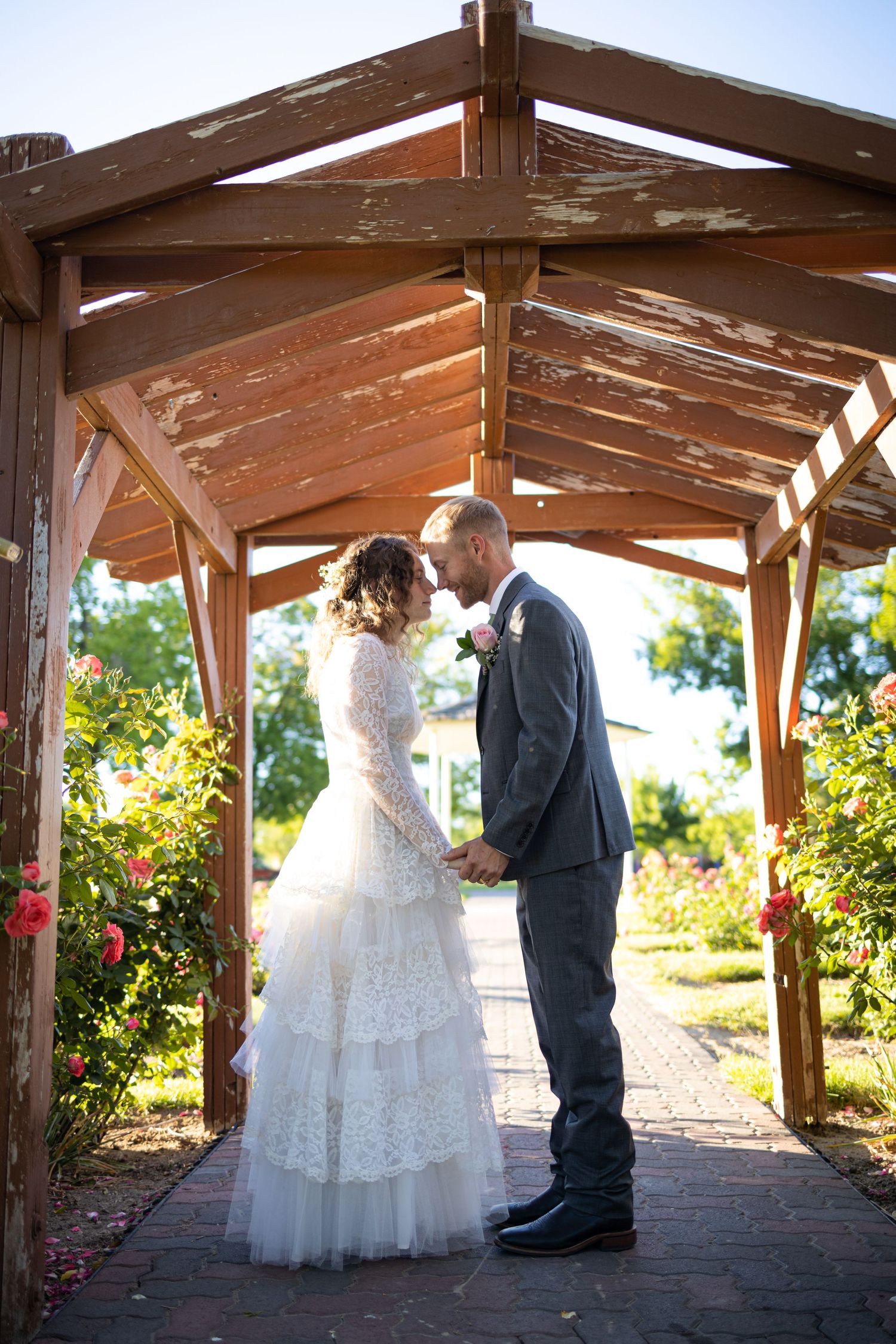 Intimate wedding ceremony moment under rustic wooden gazebo surrounded by flowers.