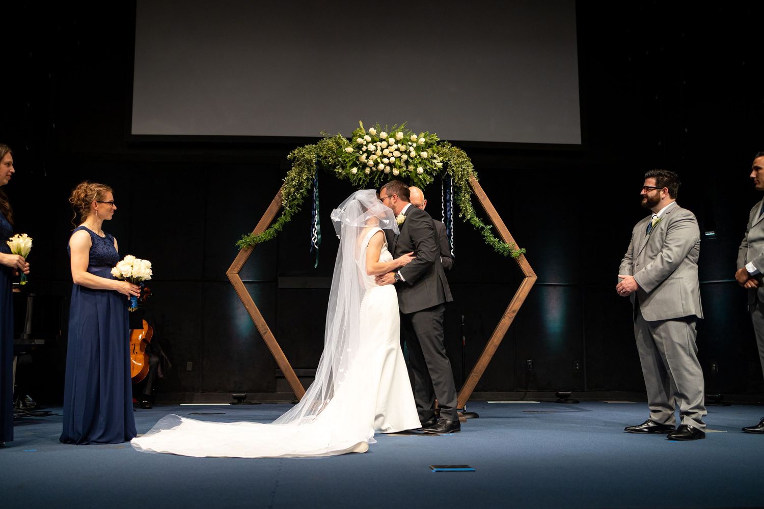 Wedding vows being exchanged beneath a modern geometric arch decorated with white flowers.