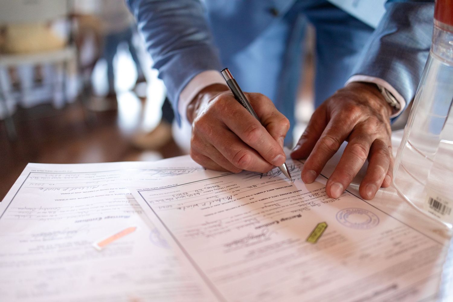 Close-up of hands signing wedding documents on white paper.